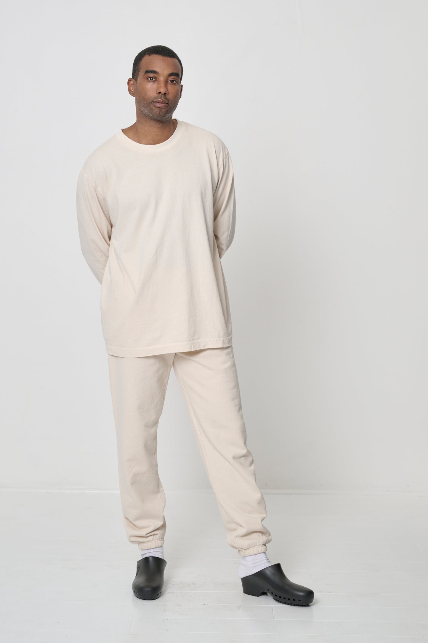 Full length of a man in a Scour Long Sleeve Trash Tee, arms crossed behind him, highlighting relaxed fabric drape.