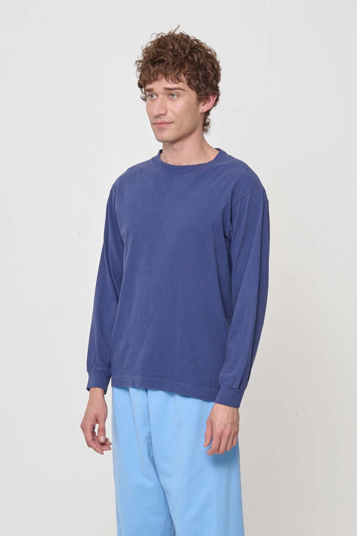 A person turned 45-degrees from the front, in a Washed Navy Long Sleeve Boxier Trash Tee, shows relaxed sleeves and rib cuff.