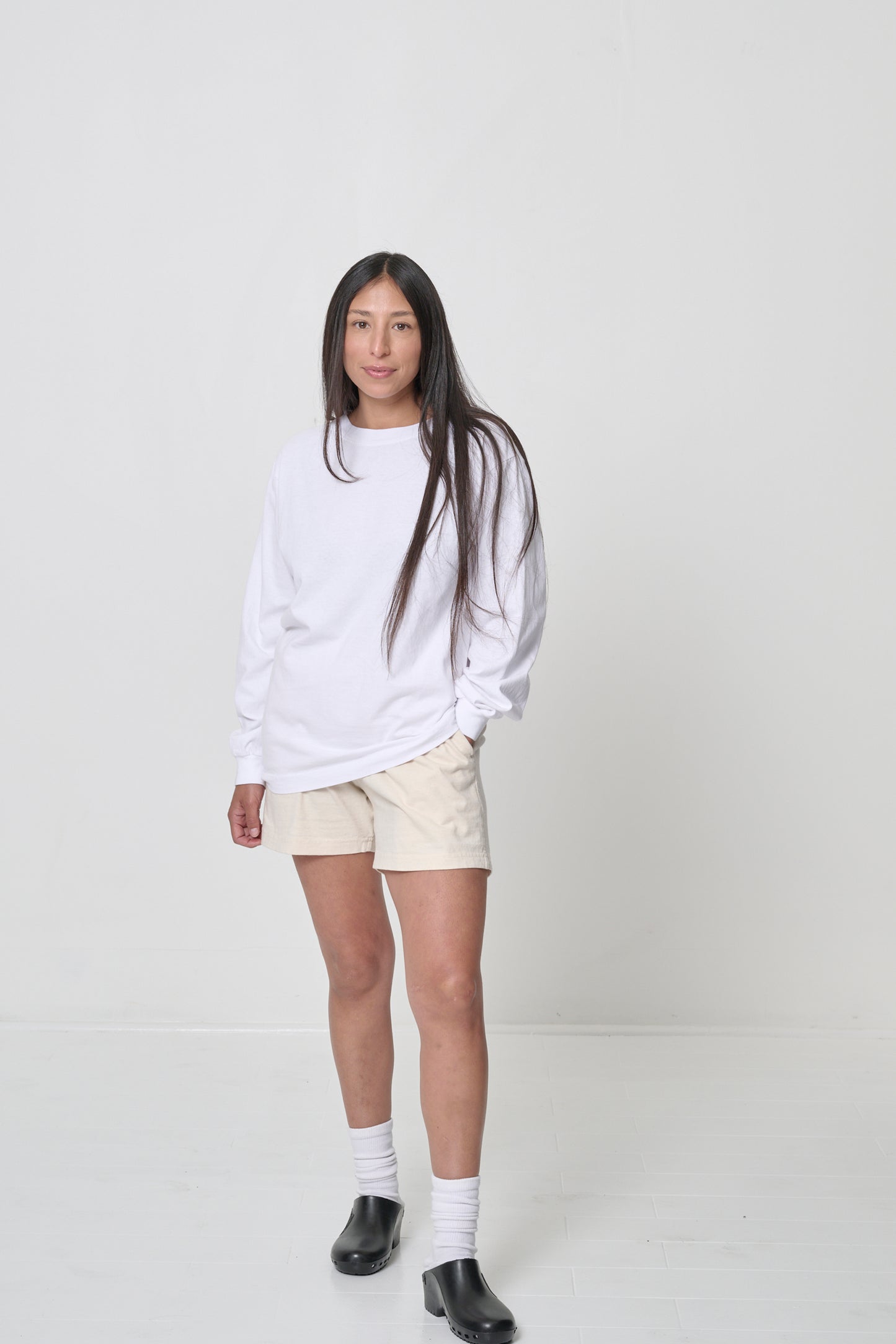 Woman in a White Long Sleeve Trash Tee and Everyday Shorts, hand in pocket, showcasing the shirt's soft drape.