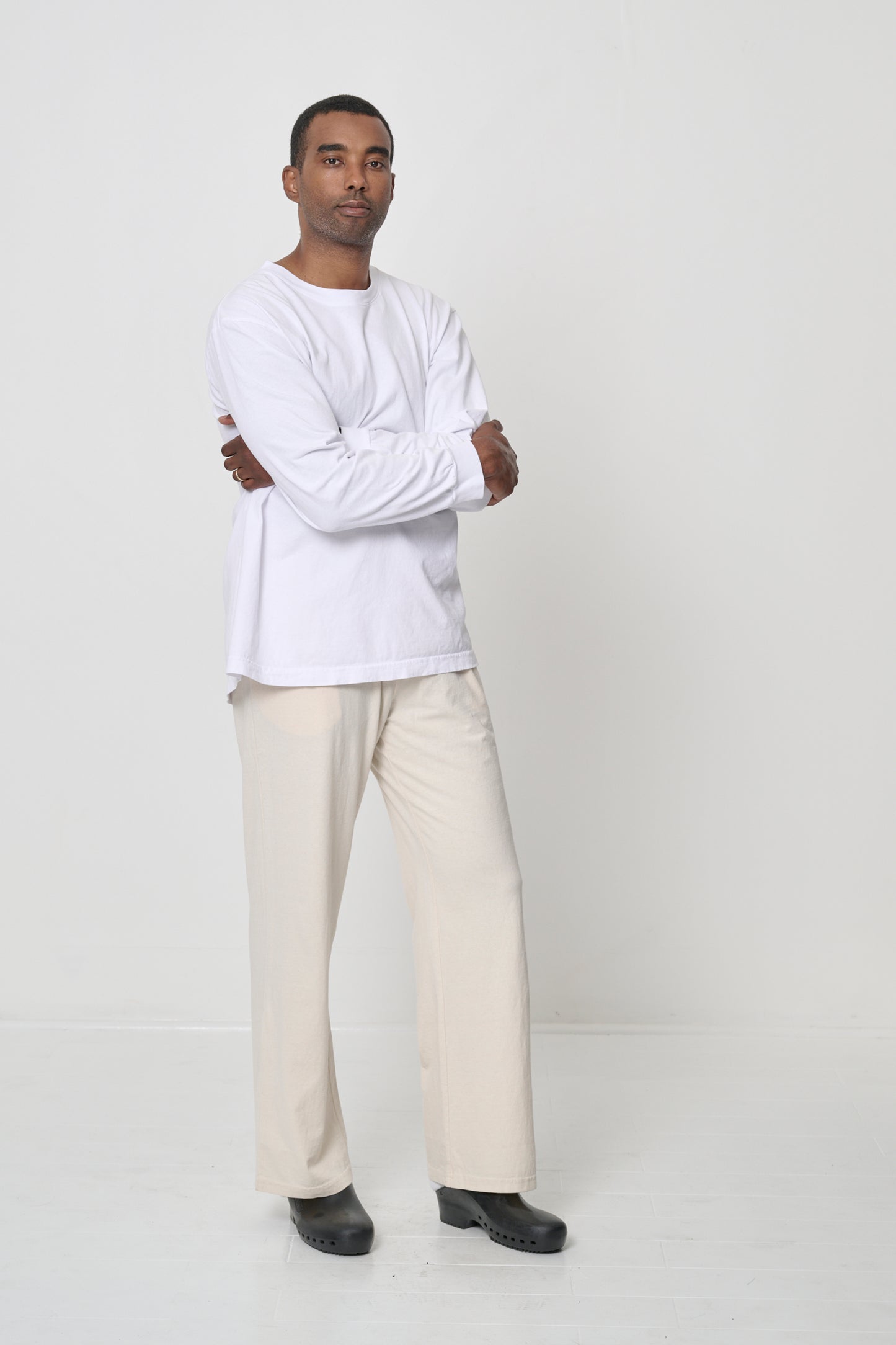Full length of man wearing a White Long Sleeve Trash Tee, arms crossed in front, showing soft drape of shirt's fabric.