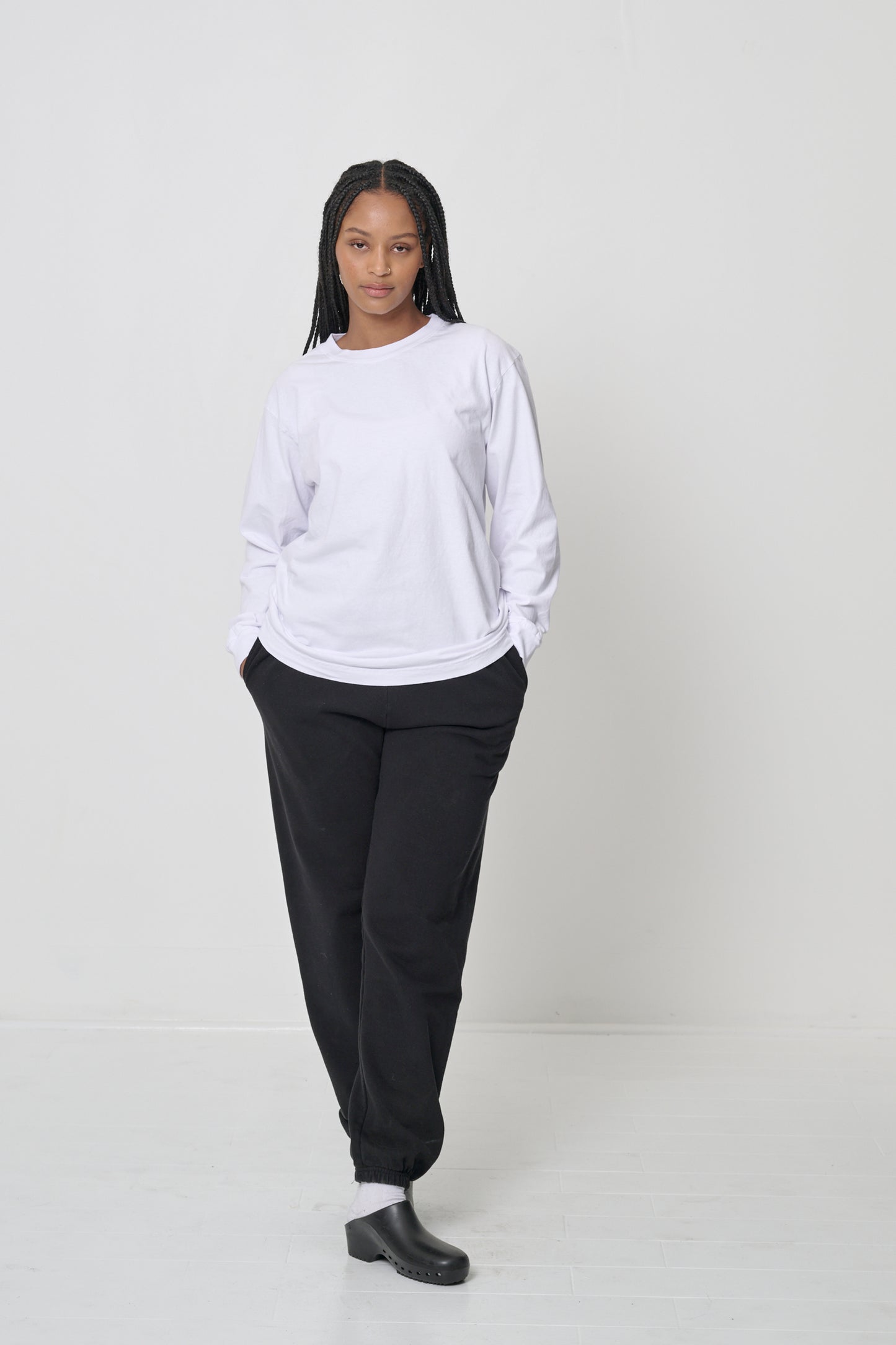 Full length of woman wearing a White Long Sleeve Trash Tee, with hands in her sweatpants pockets. Shows soft drape of shirt's fabric.