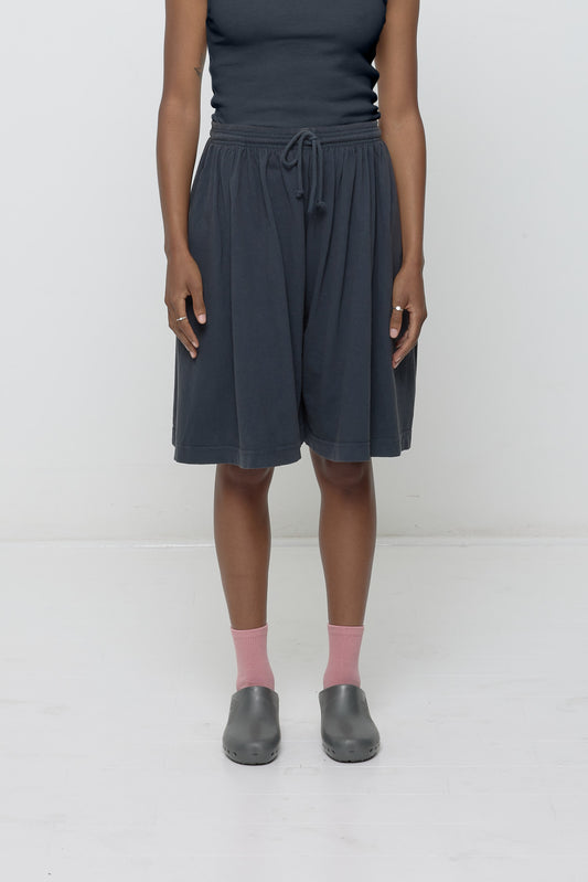 Front view of a person wearing Long Tubular Shorts in Slate dark grey, paired with a matching ribbed shirt. The shorts have a wide, relaxed leg.