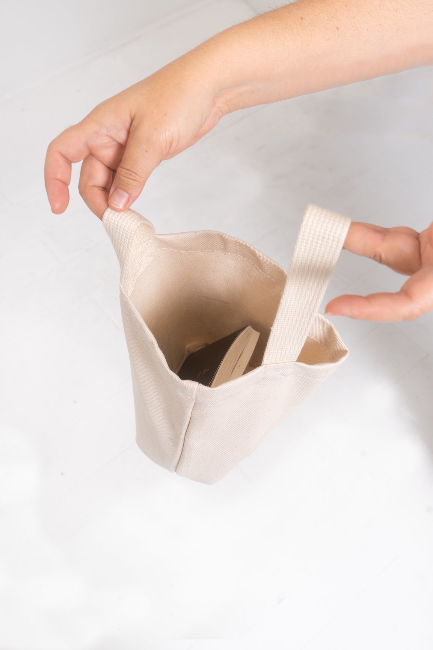 Overhead view of a Loop Tote in Natural, held open by two hands. The bag comfortably fits a book with plenty of room to spare.
