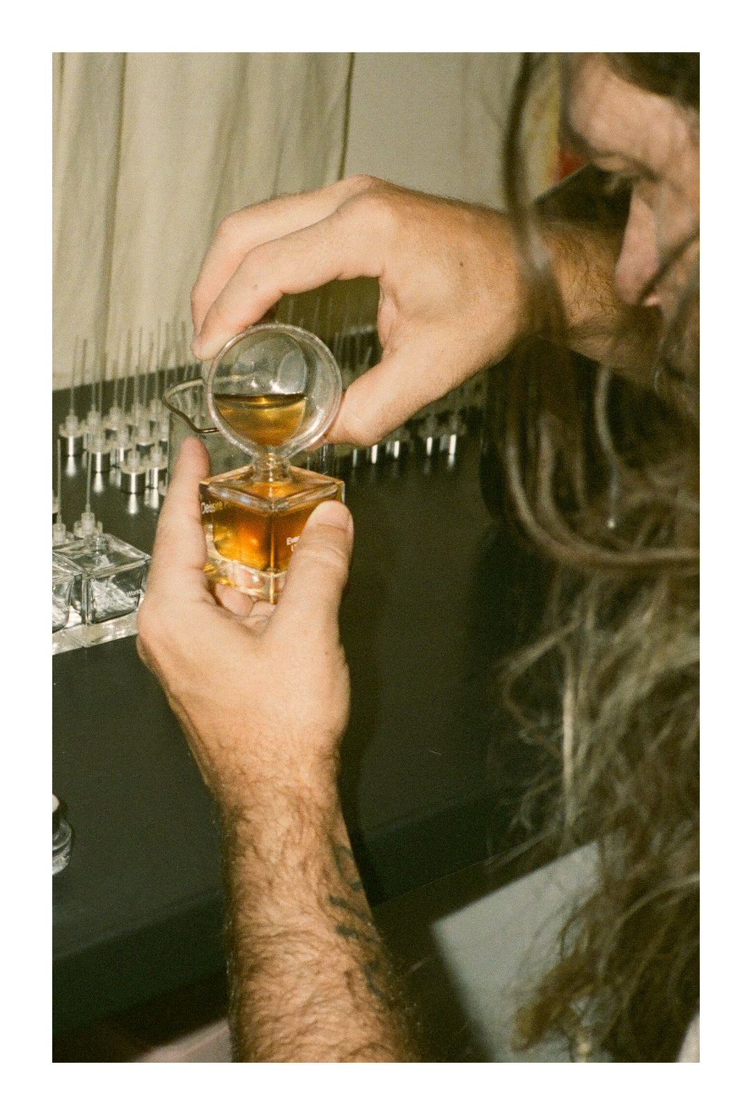 Hands pouring perfume into a Desire Path bottle. Top portion of pourer's face is in frame.