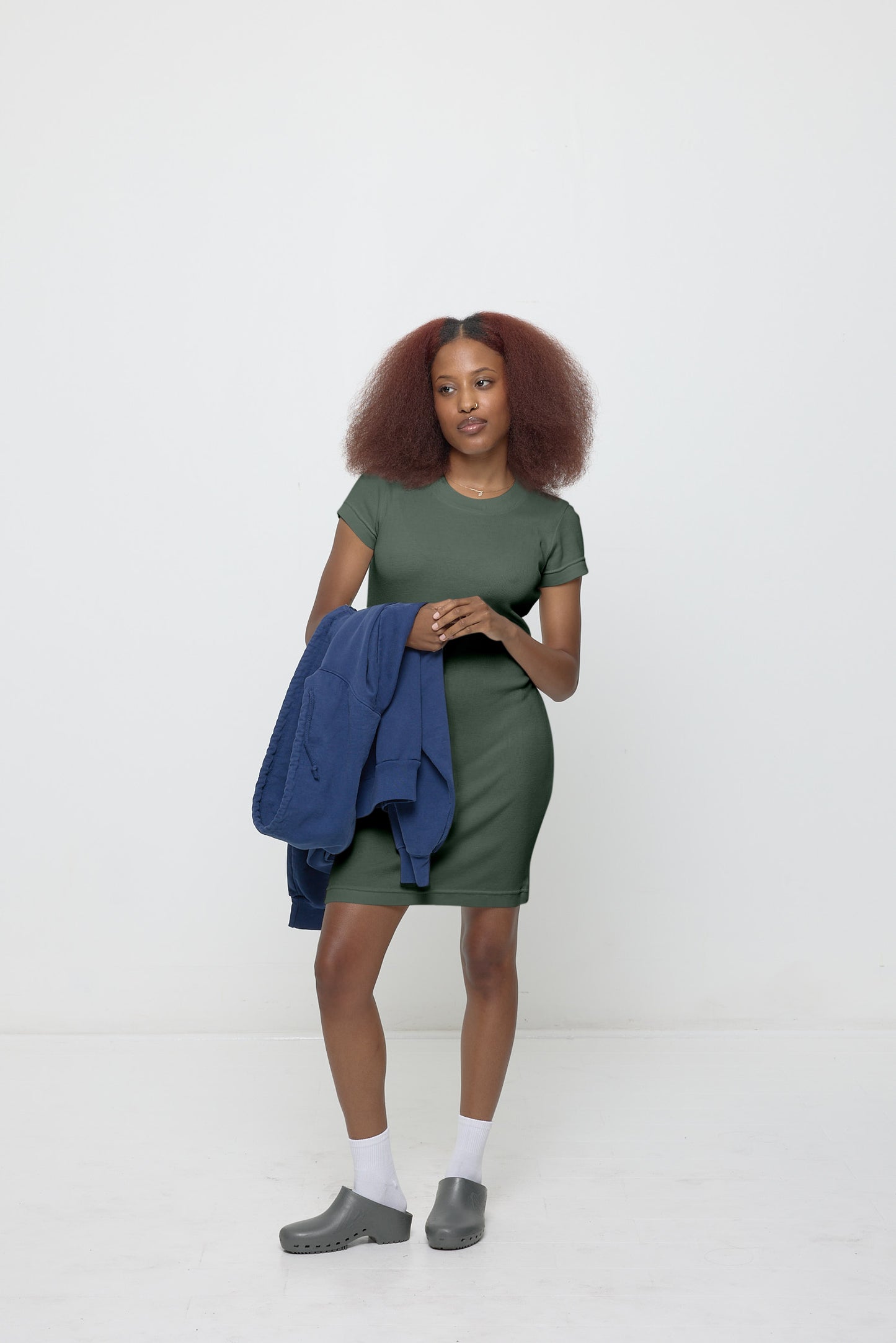 A woman wearing a Pine Rib Dress styled with a Washed Navy Trash Zip Up Hoodie slung over one arm.