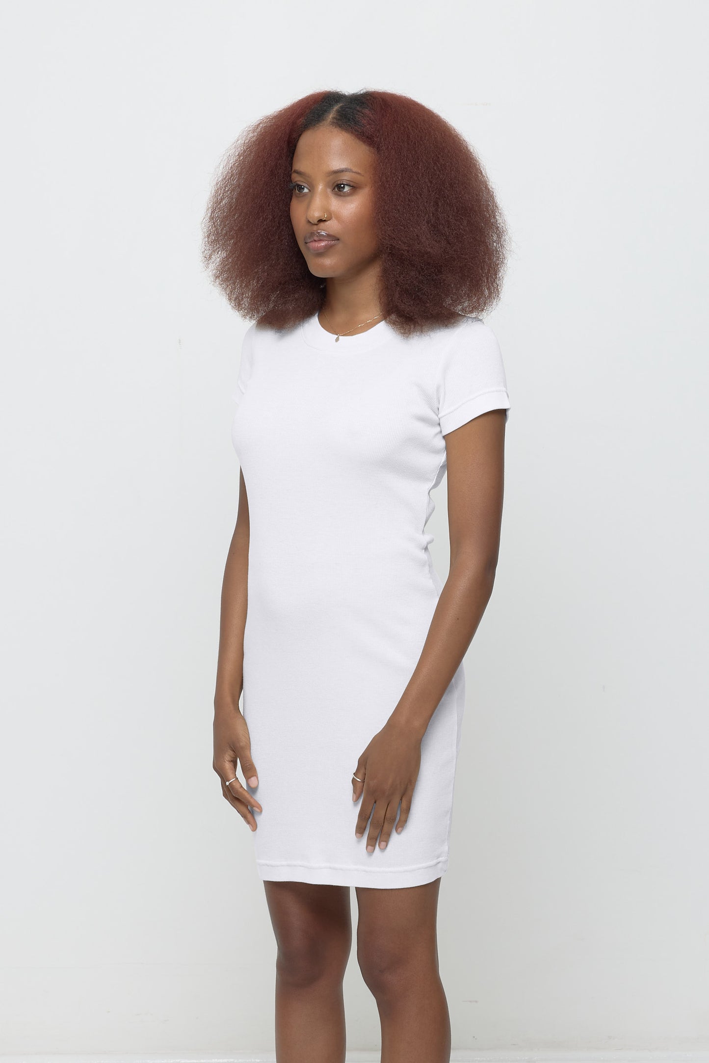 Woman turned 45-degrees from the front, in a White Rib Dress. Shows side seams, heavy hem, and fitted silhouette.