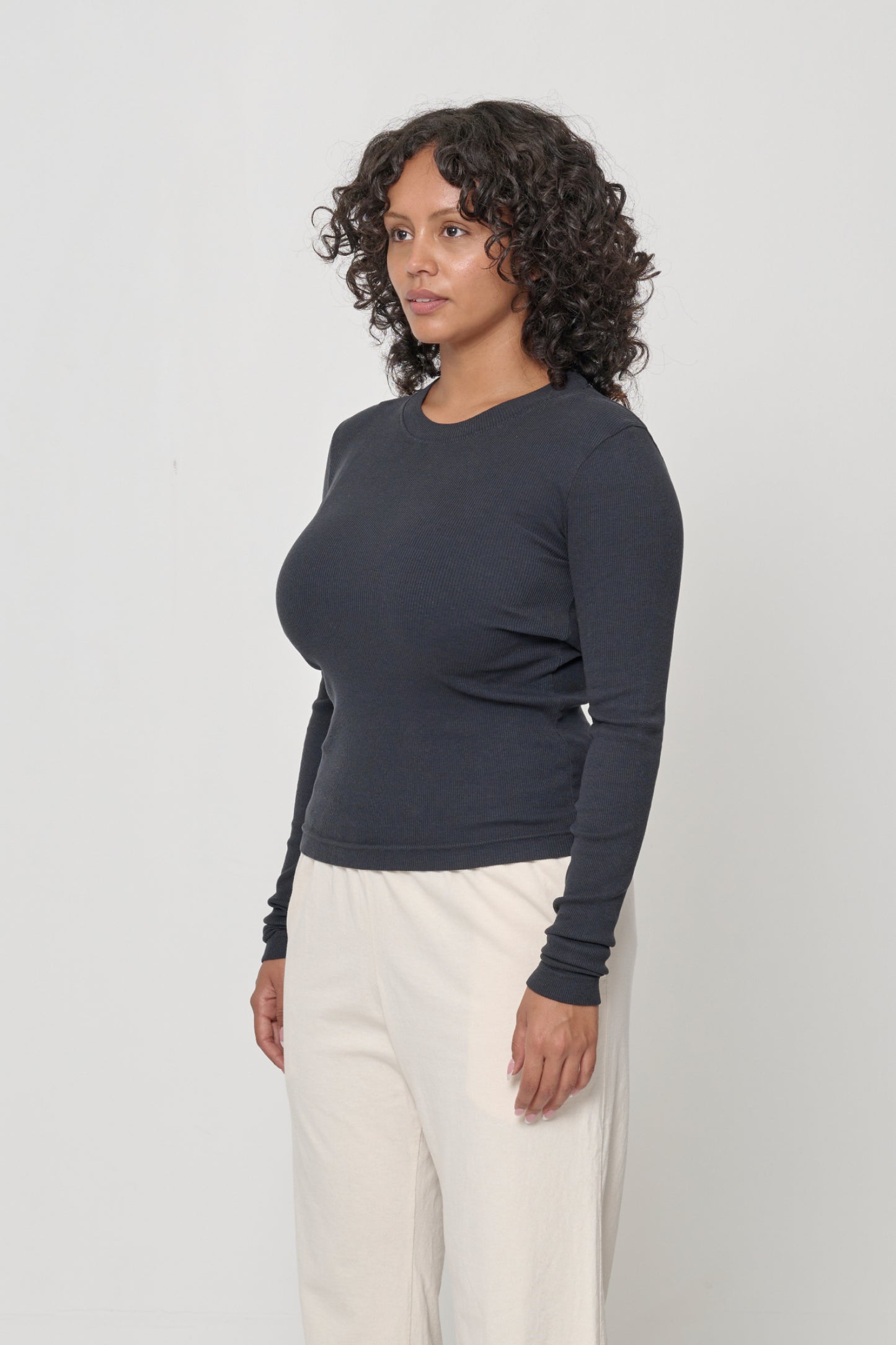 A woman turned 45-degrees from the front, in a Slate Rib Long Sleeve. Shows side seams, heavy hem, fitted silhouette.