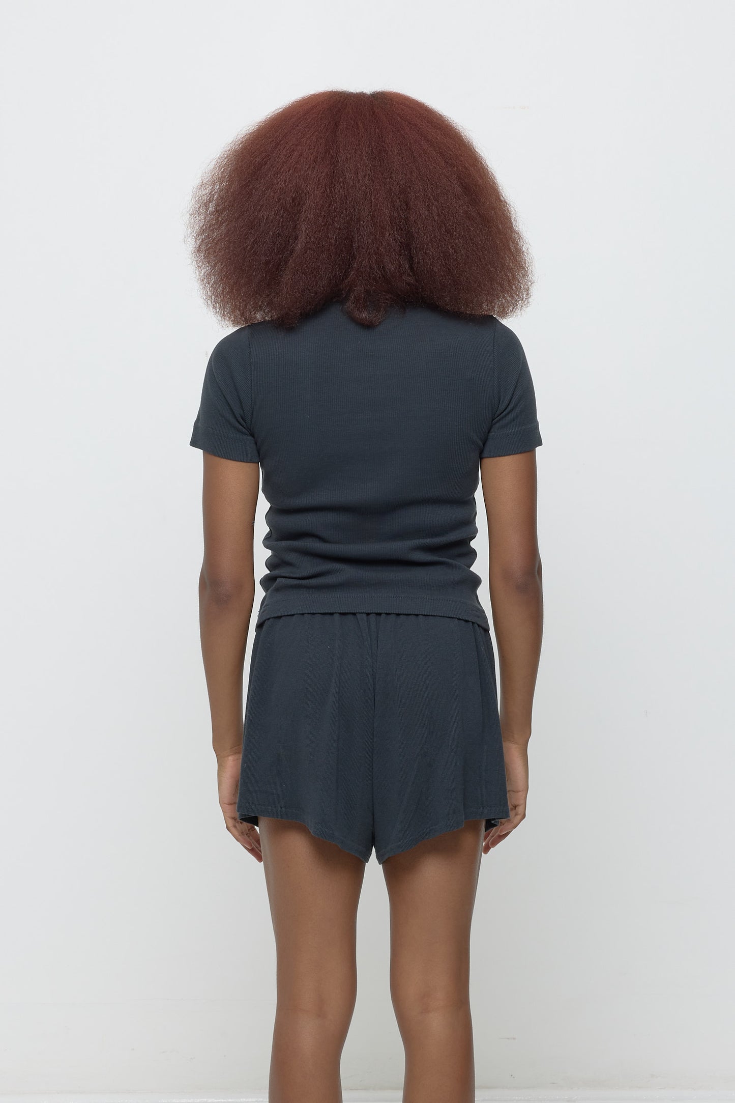 Back view: woman in Slate Rib Short Sleeve, fitted upper back, relaxed mid/lower back.