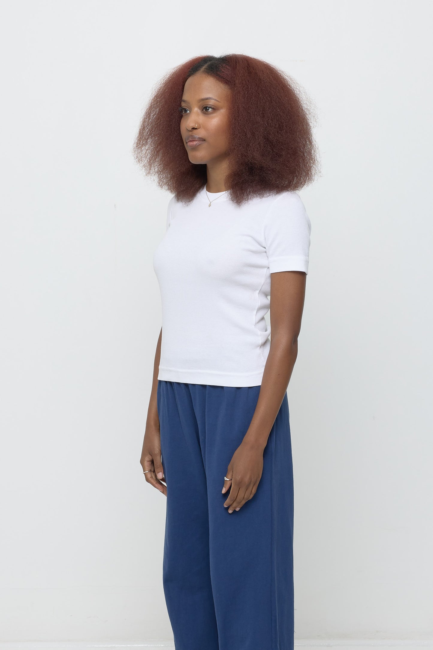 A person facing 45-degrees, wearing a White Rib Short Sleeve, showcasing side seams, heavy hem, and fitted silhouette.