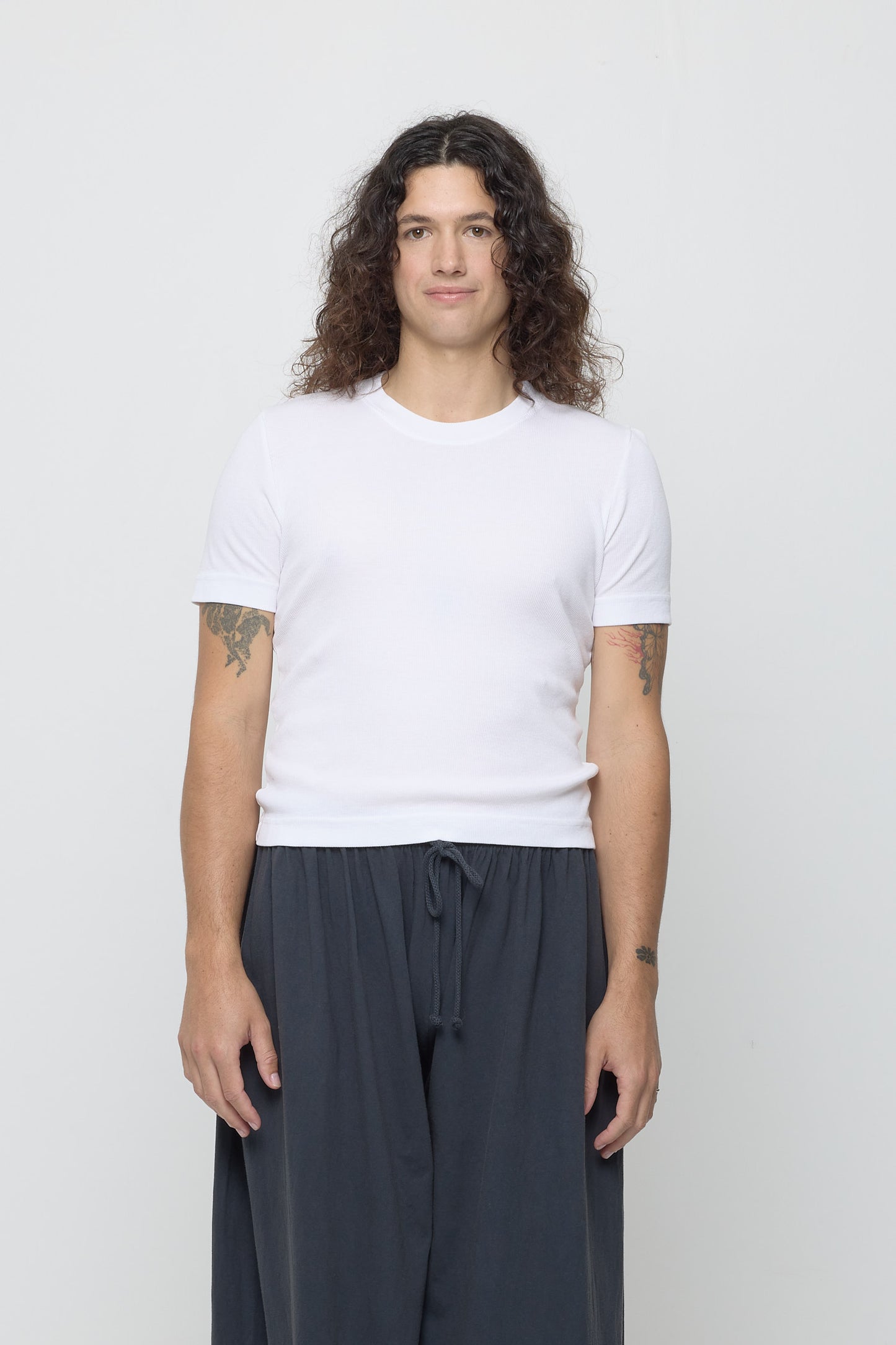 Front view of a 6' person wearing a size XL Rib Short Sleeve in White. Hem rests just above their hips.