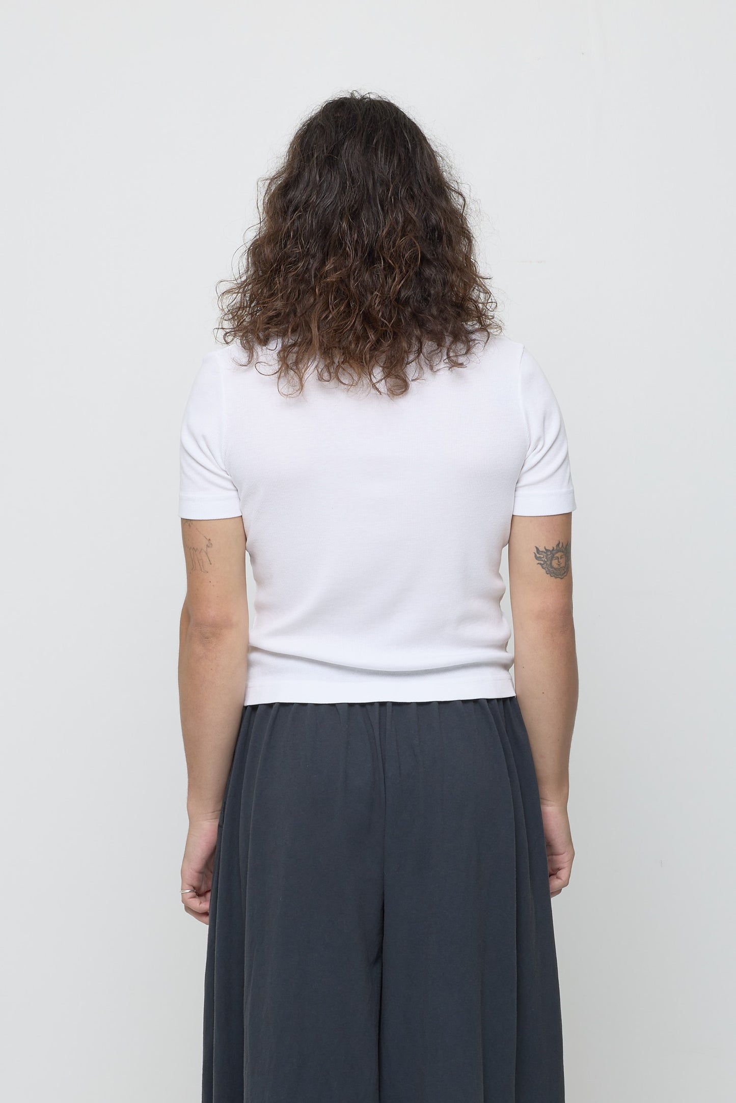 Back view: a person in a White Rib Short Sleeve, fitted upper back, relaxed lower back.