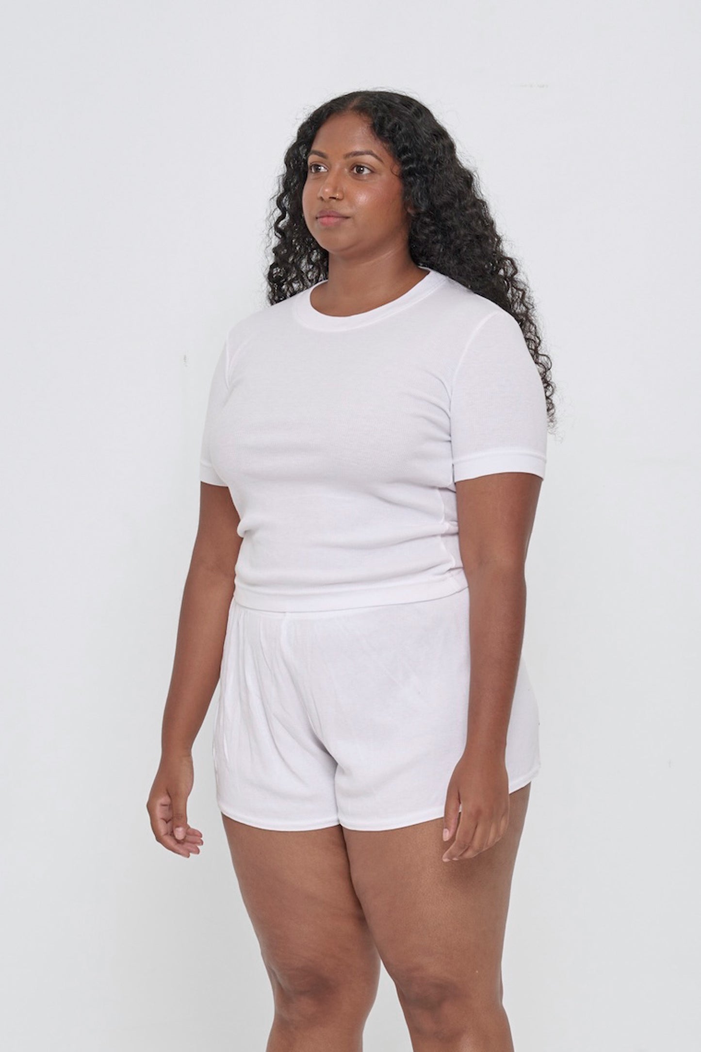A person facing 45-degrees, wearing a White Rib Short Sleeve, showcasing side seams, heavy hem, and fitted silhouette.
