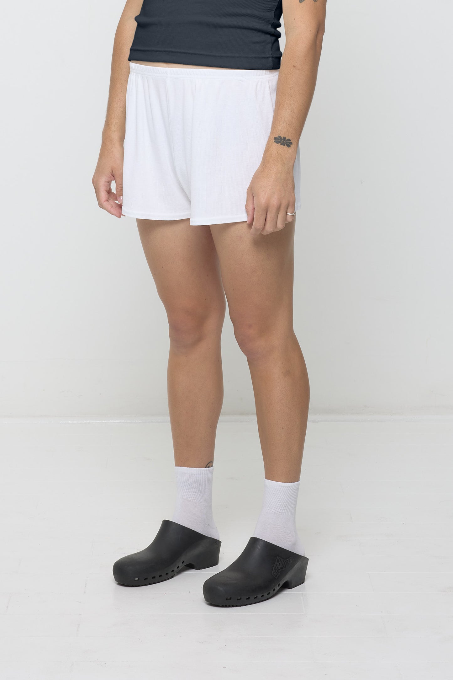 A person facing 45-degrees, wearing White Rib Shorts, showcasing spacious leg openings.