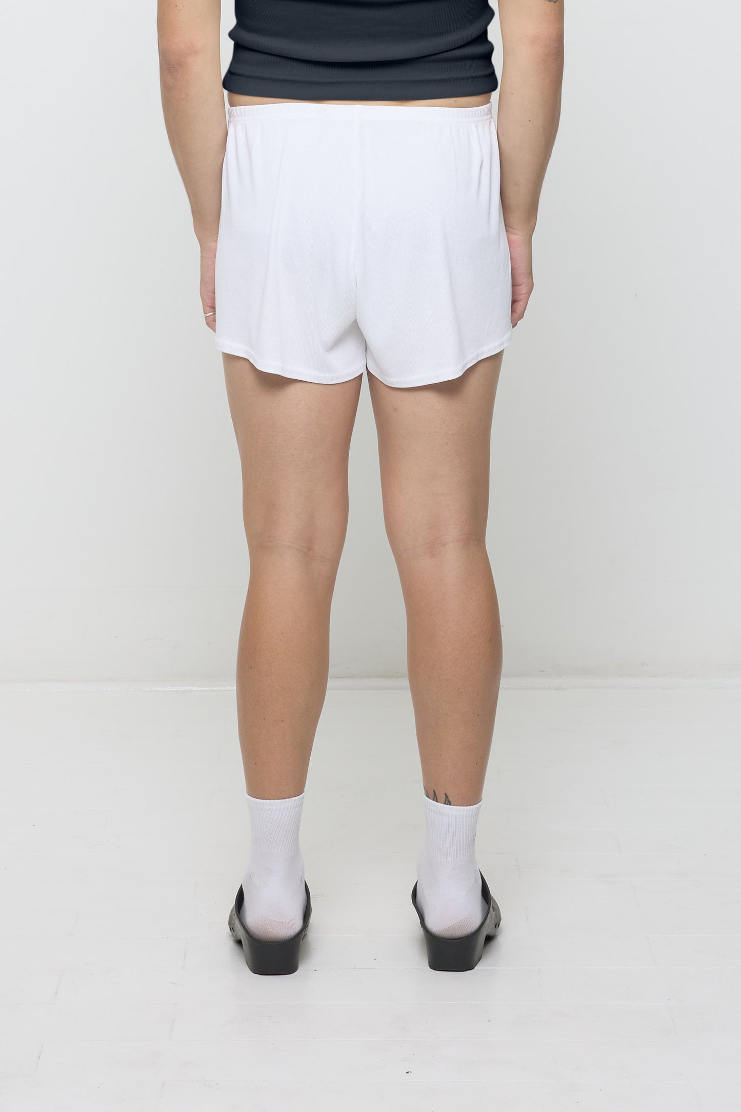 Back view: White Rib Shorts on a person, waist down. They feature a relaxed fit and a flowing, drapey fabric.