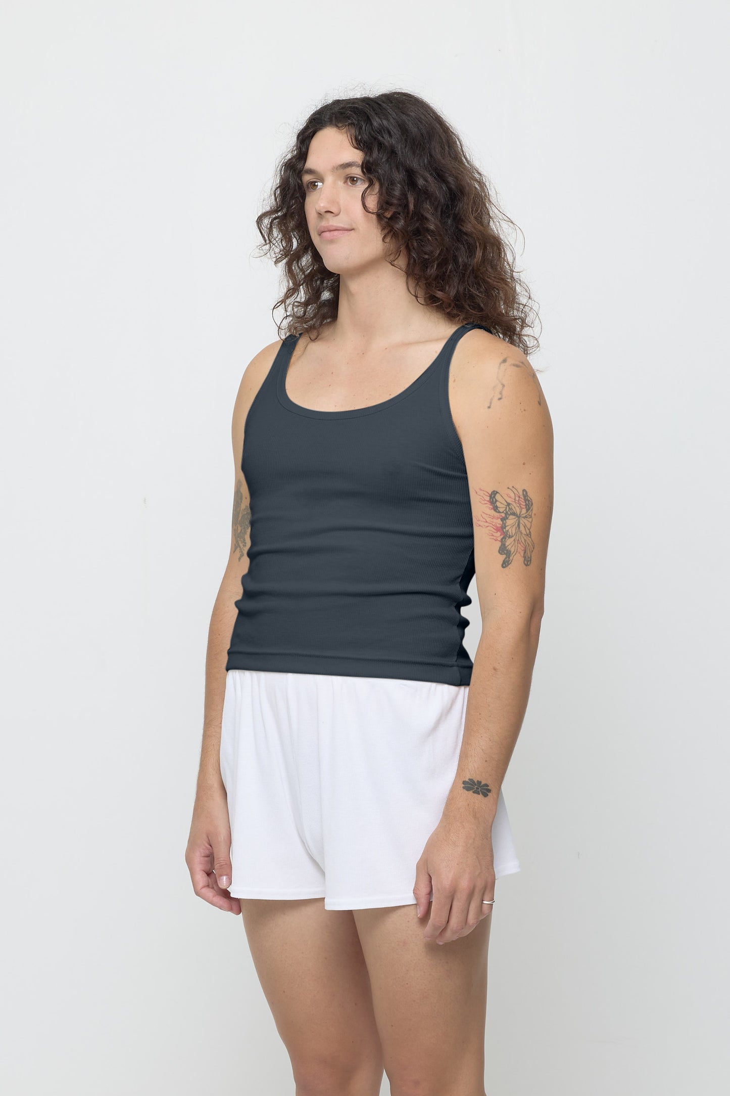 A person facing 45-degrees, wearing a Slate Rib Tank, showcasing side seams, heavy hem, and fitted silhouette.