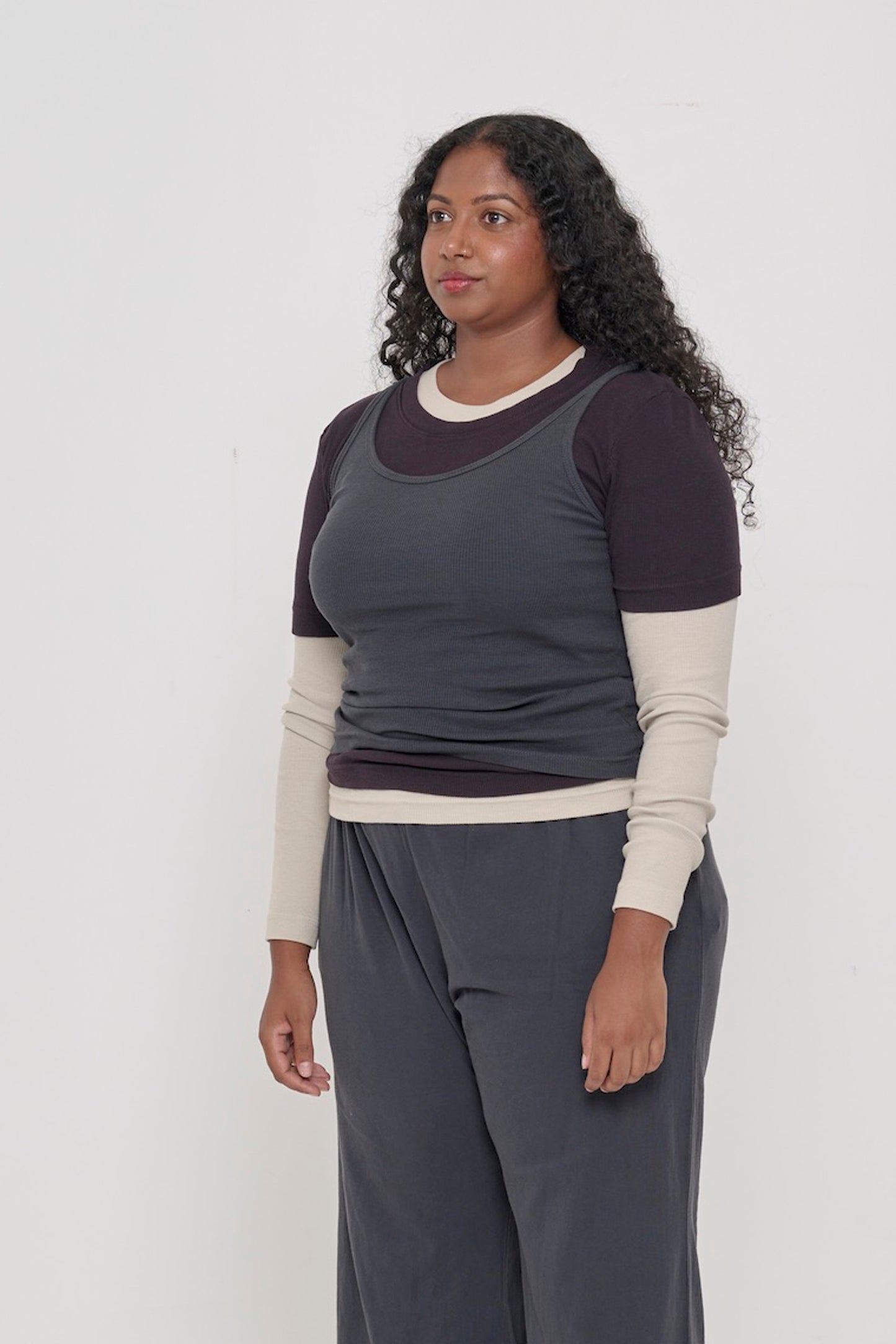 A person facing 45-degrees, wearing a Slate Rib Tank, showcasing heavy hem, and fitted silhouette.