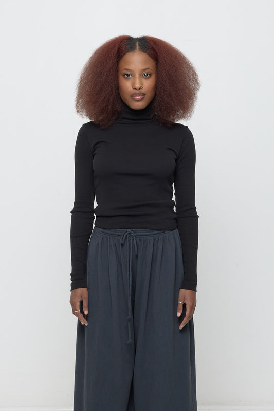 A 5'3" woman wearing a size S Rib Turtleneck in Black. Hem rests on her upper hips.