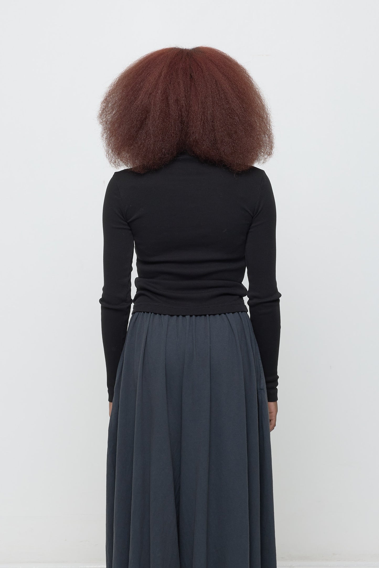 Black Rib Turtleneck, back view on a woman. Fitted through upper back, looser mid to lower back.