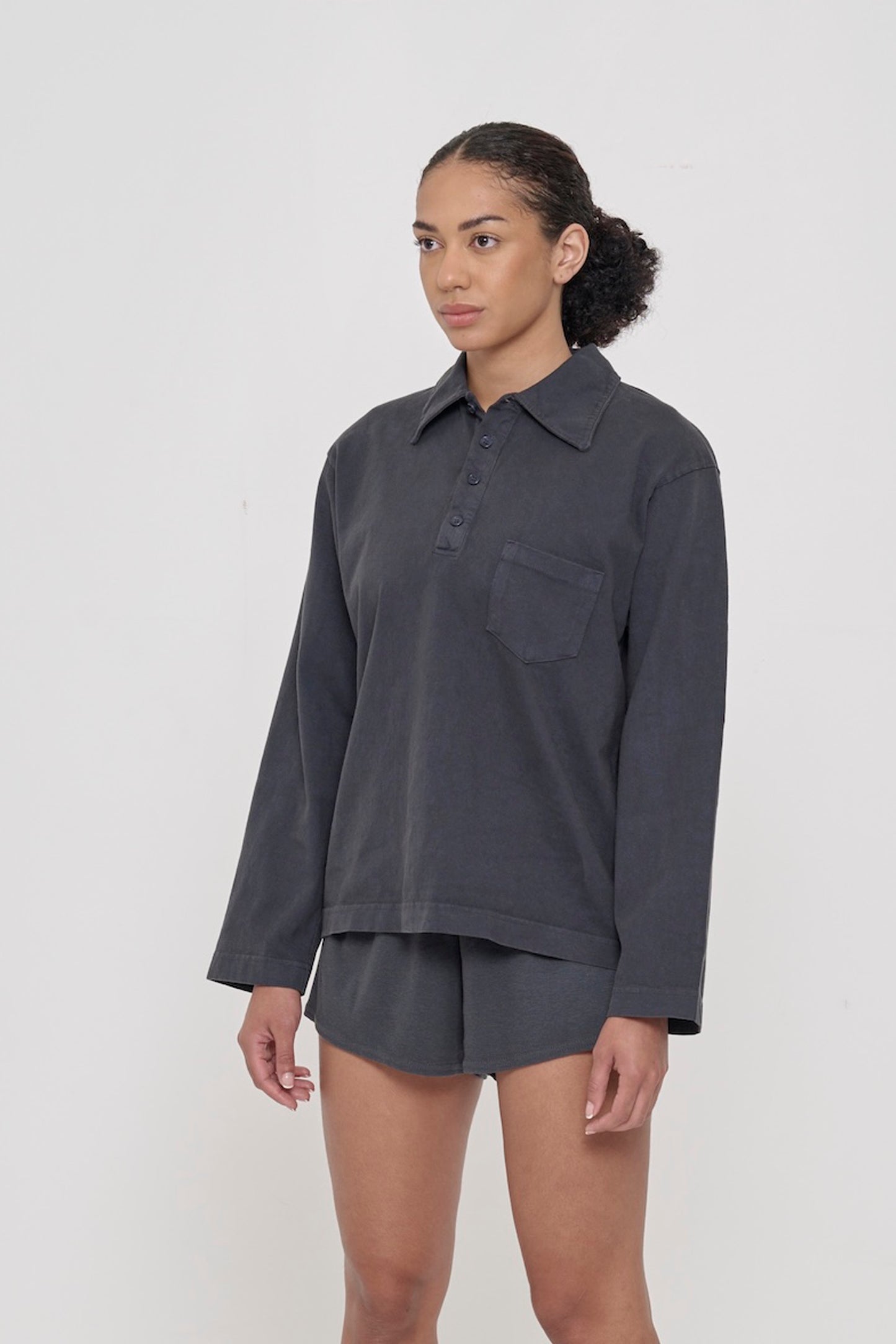 Woman turned 45 degrees, wearing a Slate Rugby Trash Polo, showing relaxed straight sleeves.