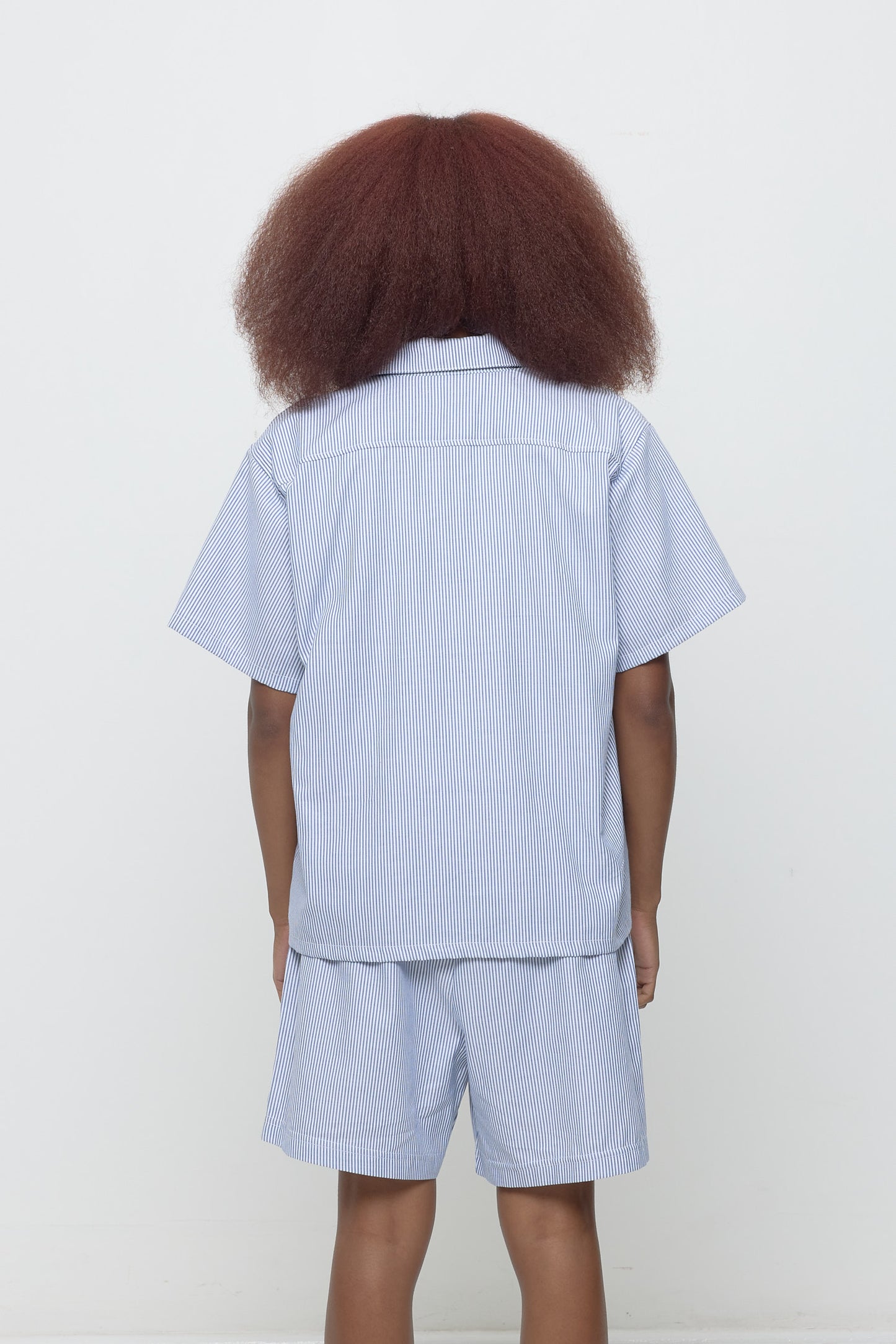Back view: A 5'3" woman in a blue Stripe Poplin Button Up Shirt, showing yoke and hem that hits just below her hips.