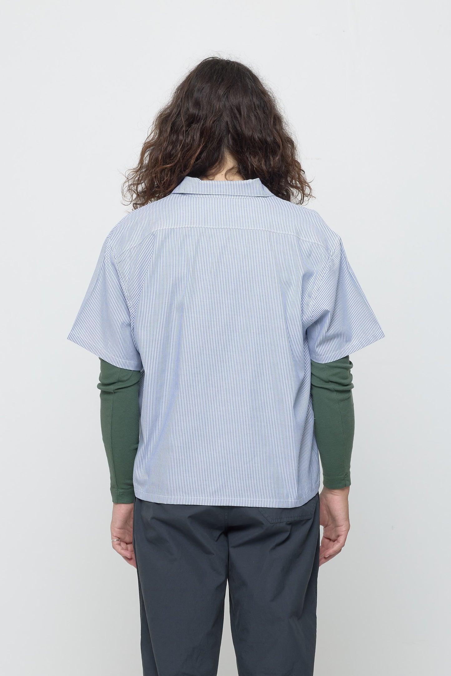 Back view: A 6' person in a blue Stripe Poplin Button Up Shirt, showing yoke and hem that hits just their lower hips.