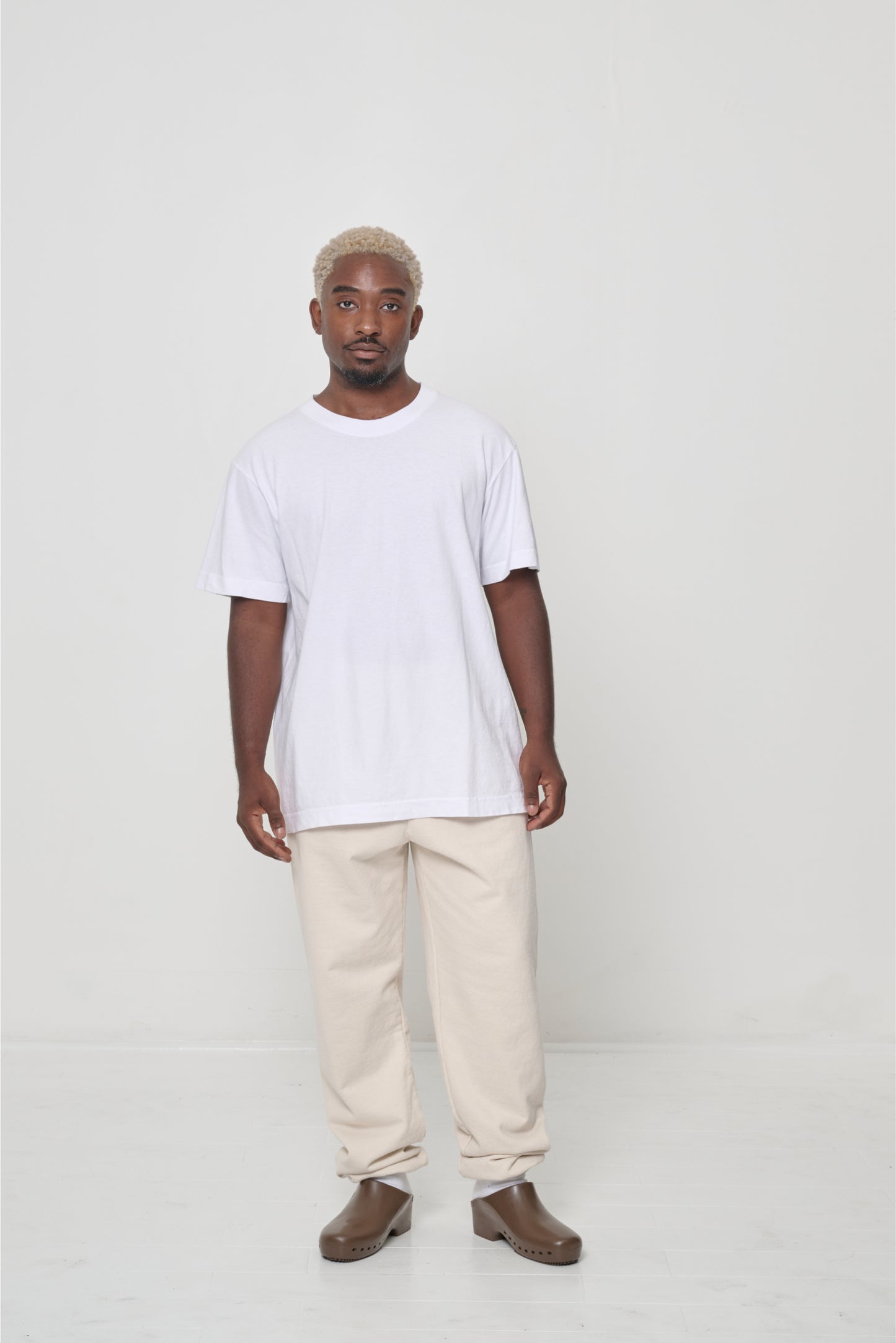 Front view: a man wearing a White Short Sleeve Trash Tee, with Scour sweatpants, showing a classic, relaxed fit.
