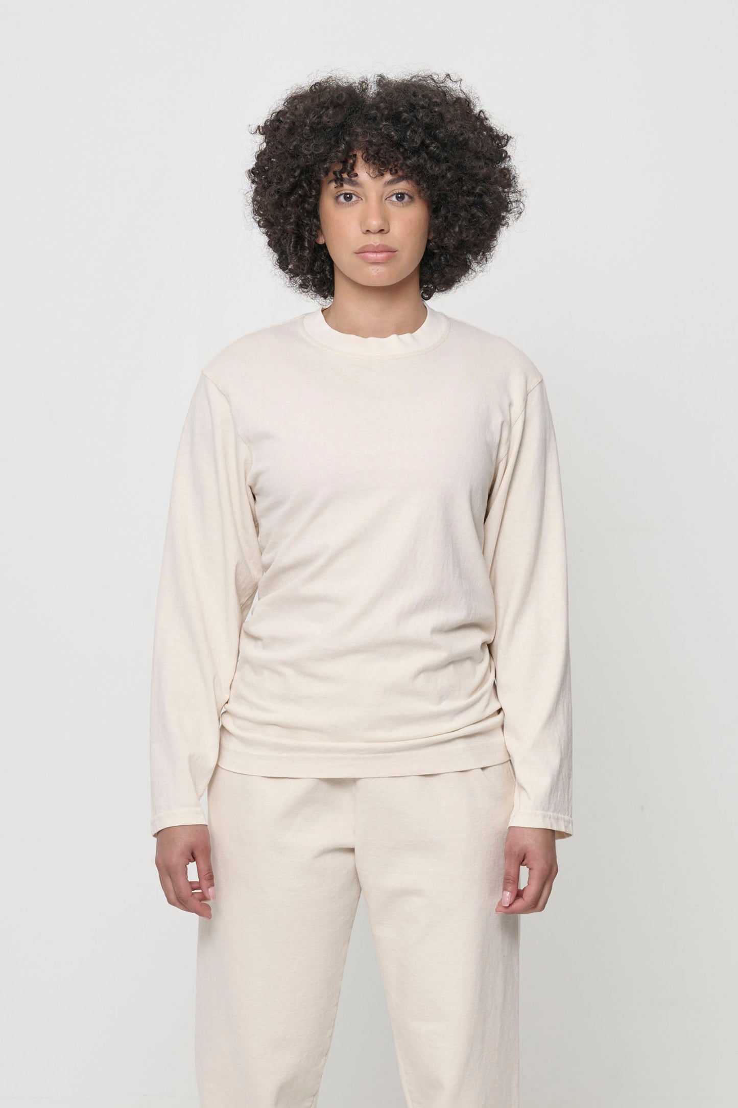 A person wearing a beige Scour Straight Sleeve Trash Tee, which has no cuffs.