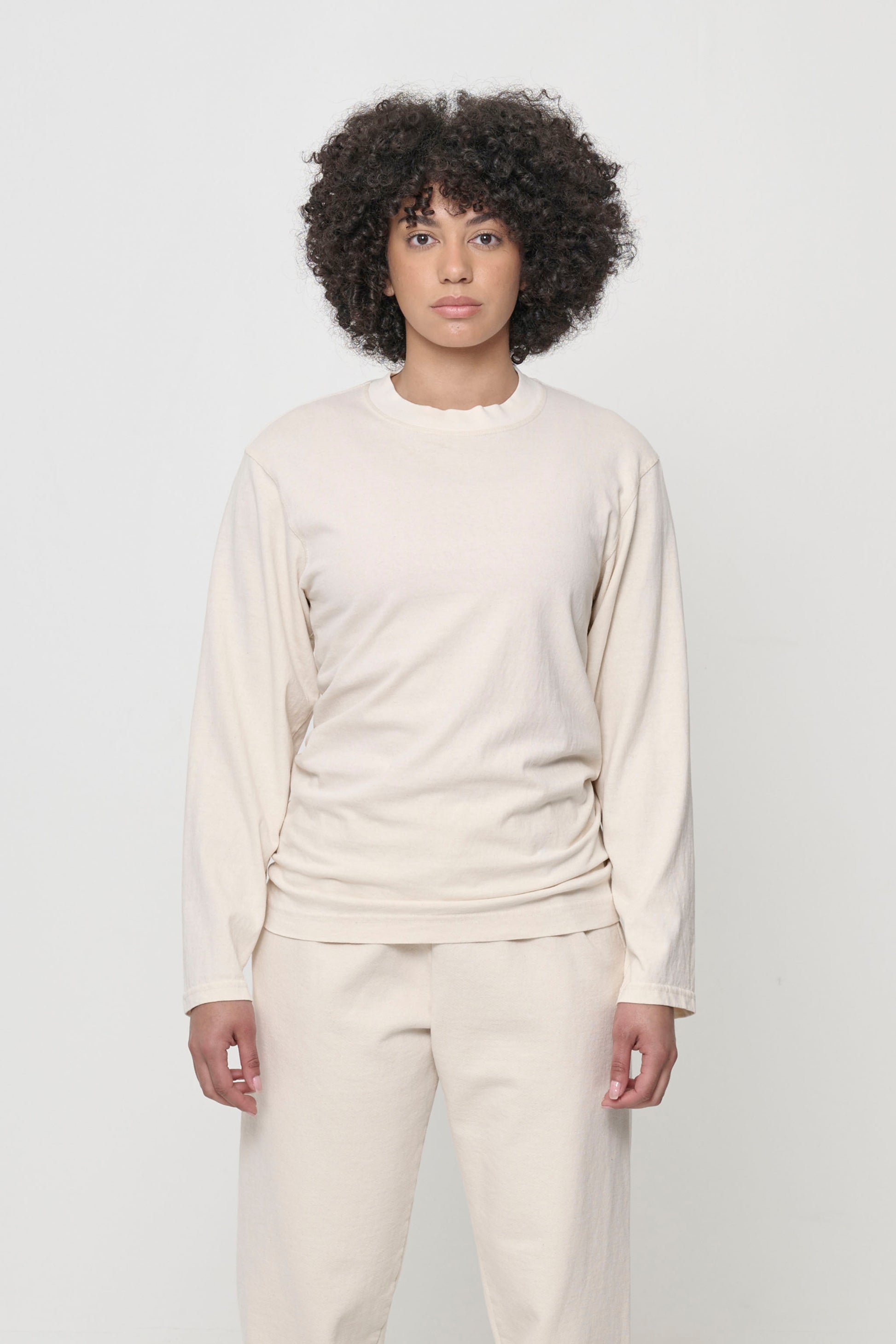 A person wearing a beige Scour Straight Sleeve Trash Tee, which has no cuffs.