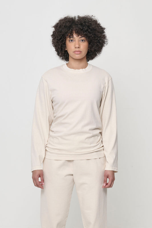 A person wearing a beige Scour Straight Sleeve Trash Tee, which has no cuffs.