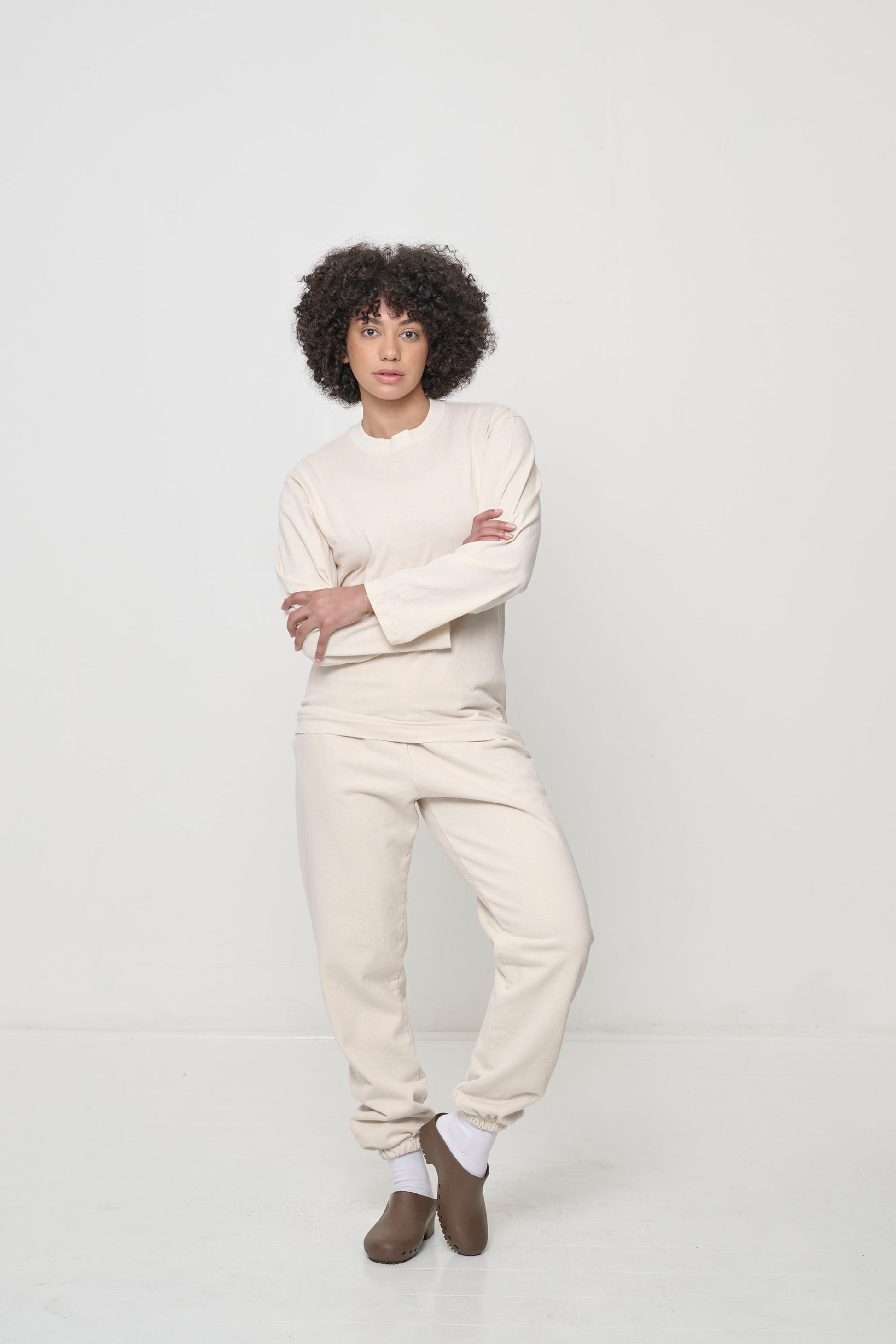 A person wearing a beige Scour Straight Sleeve Trash Tee, with arms crossed.