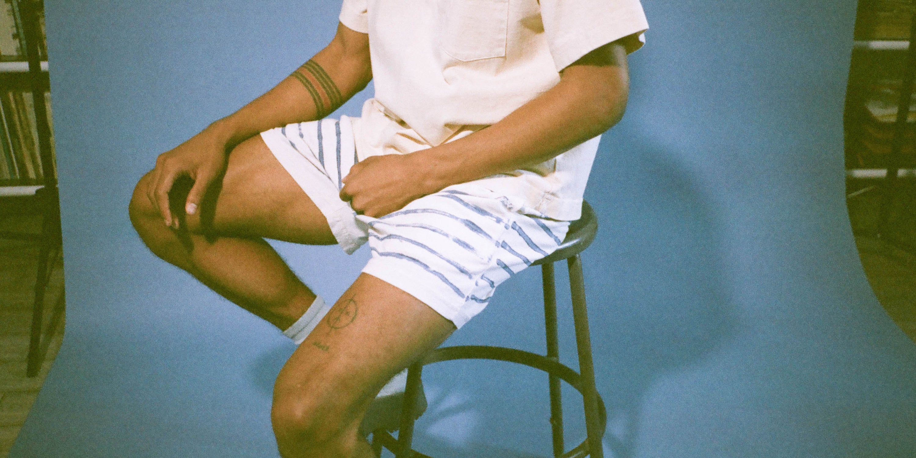 Model sits on stool wearing Stripe Everyday Shorts and a Trash Polo