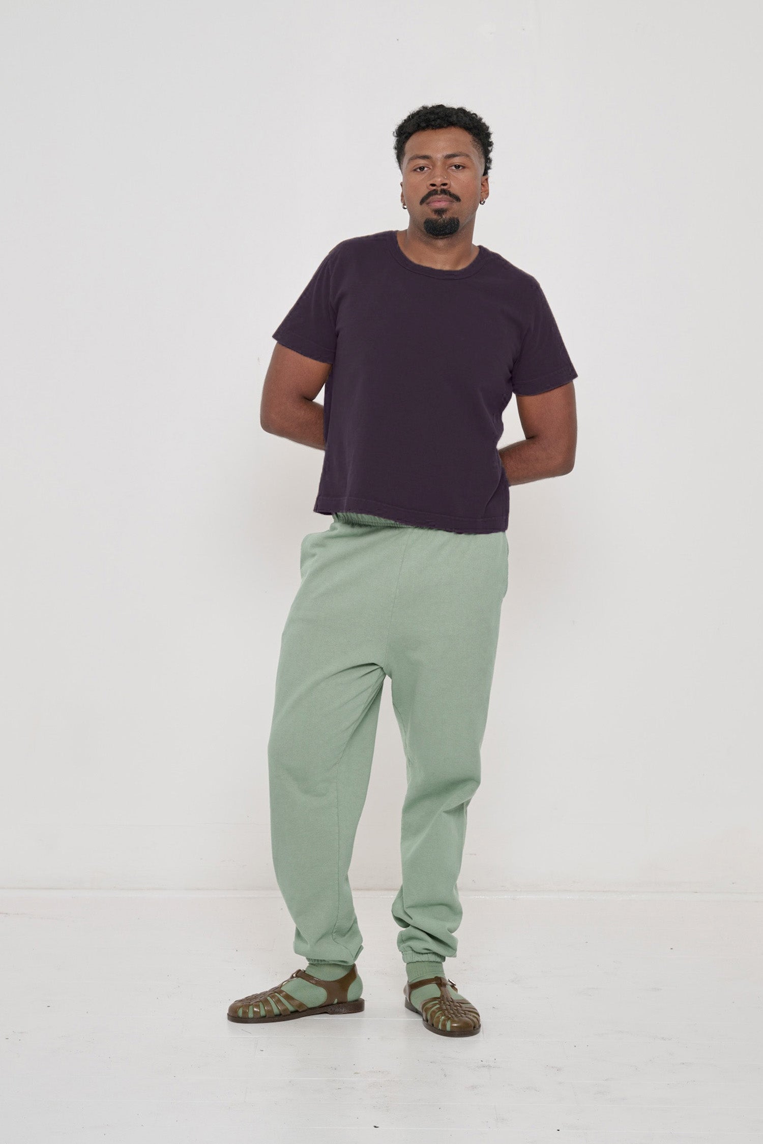 Man in Mulberry Tailored Trash Tee and Wasabi Trash Sweatpants, one hand in pocket, showing shirt's slim sleeves.