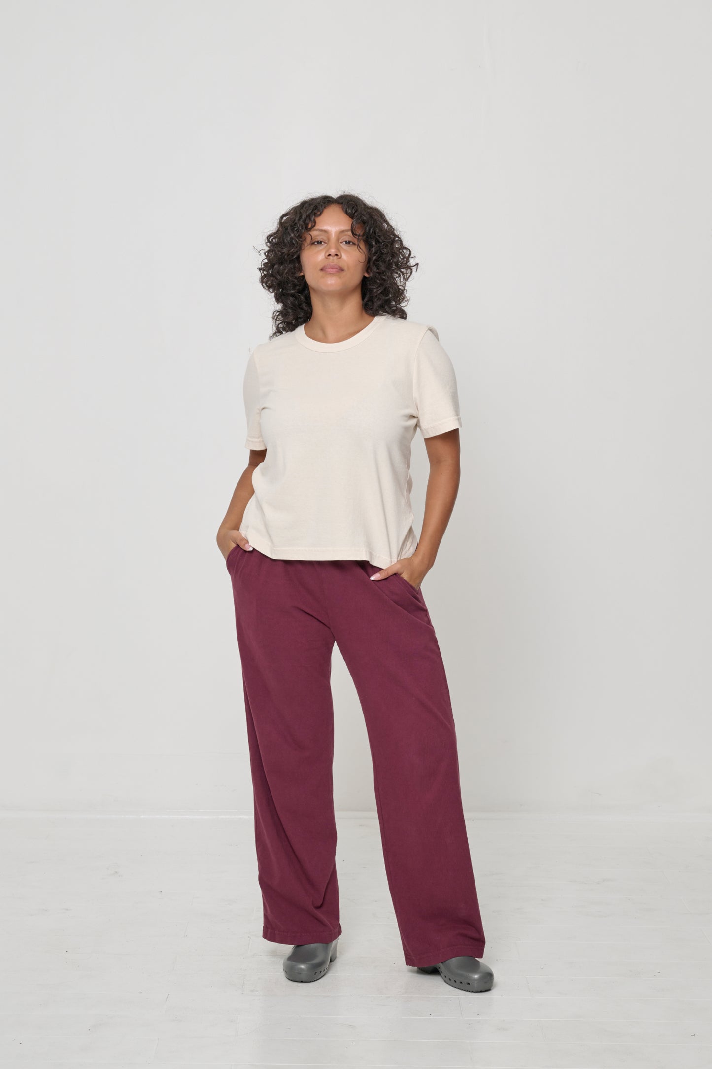 Woman wearing a Scour Tailored Trash Tee with hands in Burgundy Apartment Pants pockets, showcasing shirt's slim sleeves.
