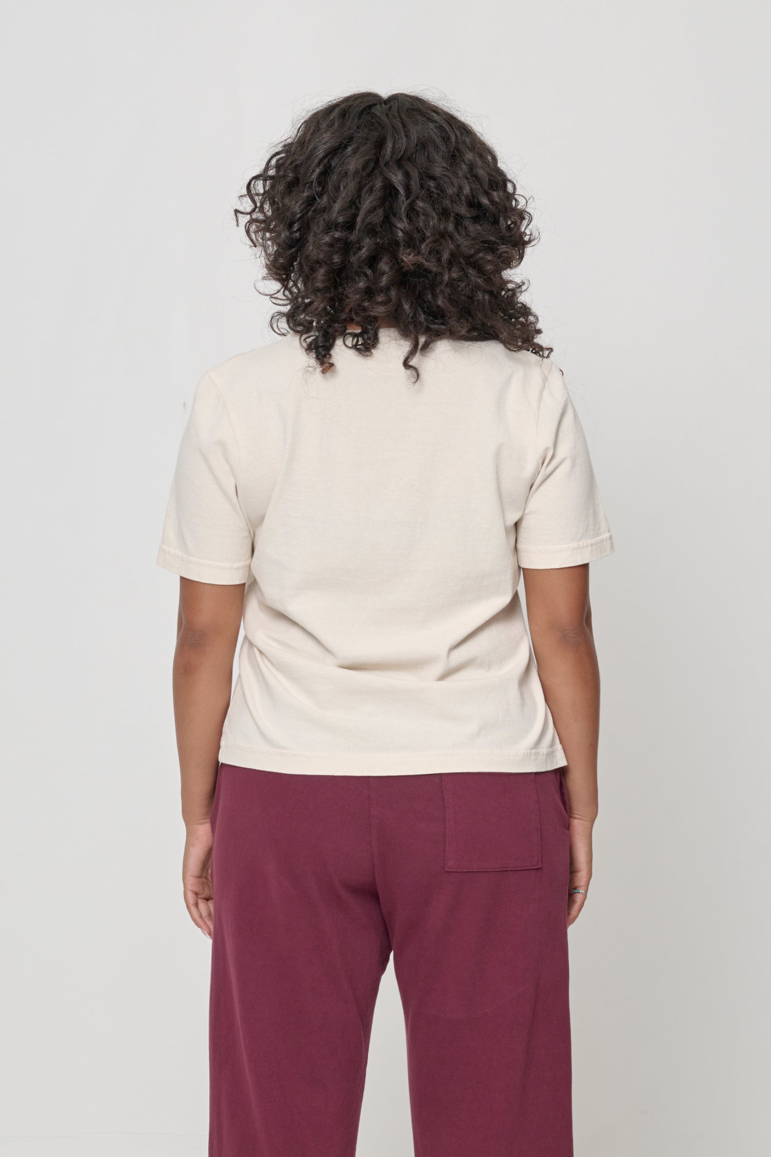 Back view: woman in a Scour Tailored Trash Tee in Scour. Nearly fitted across upper back and relaxed at middle and lower back