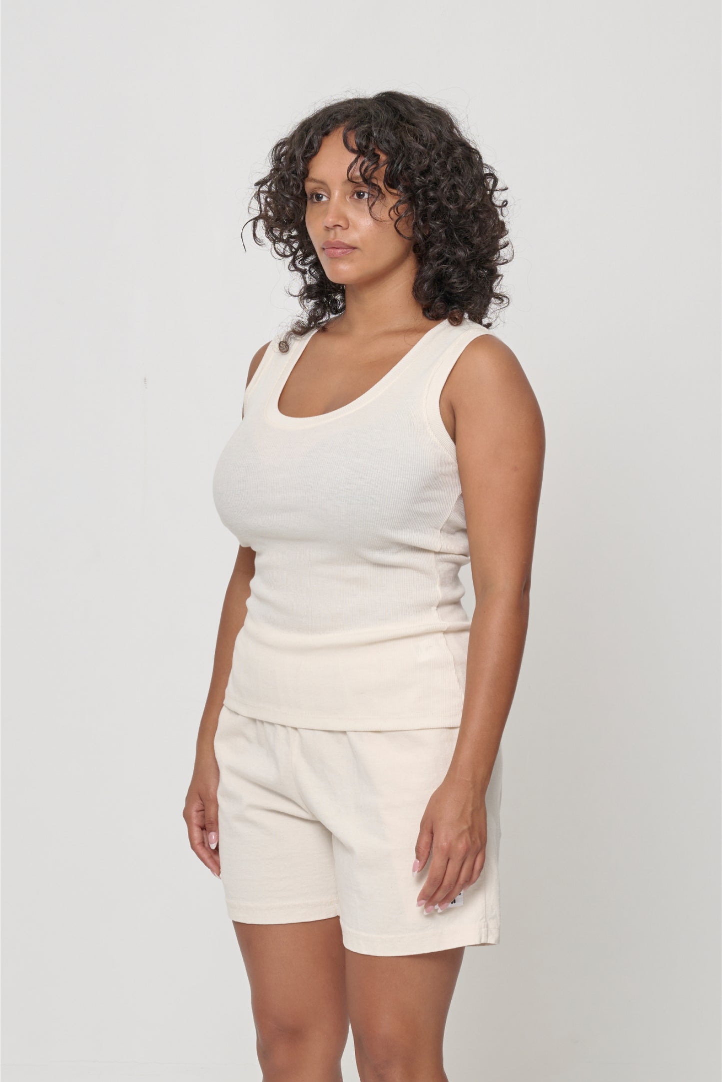 A person facing 45-degrees, wearing a Natural The Tank, showcasing side seams and fitted silhouette.