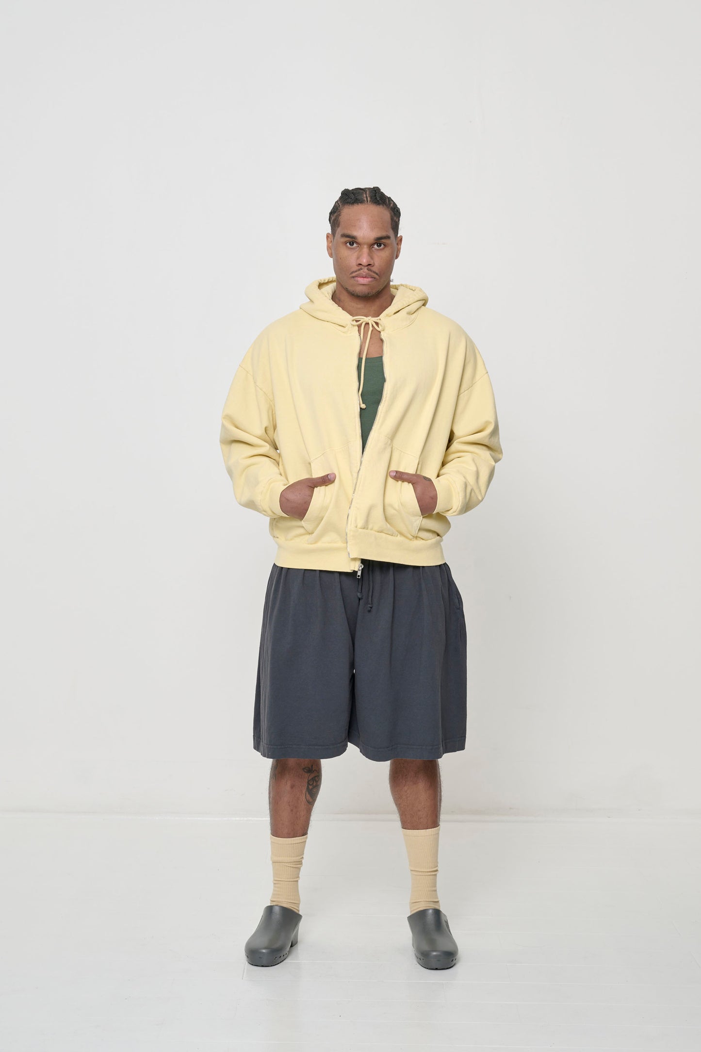 Man in a Pine The Tank, layered under a French Butter Trash Zip Up Hoodie and Slate Long Tubular Shorts.