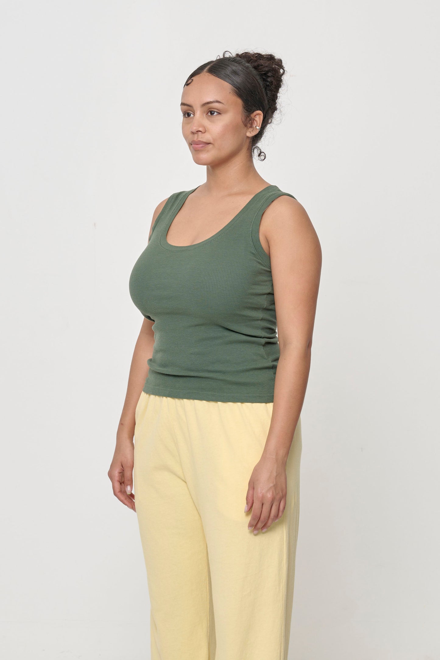 A person facing 45-degrees, wearing a Pine The Tank, showcasing side seams and fitted silhouette.