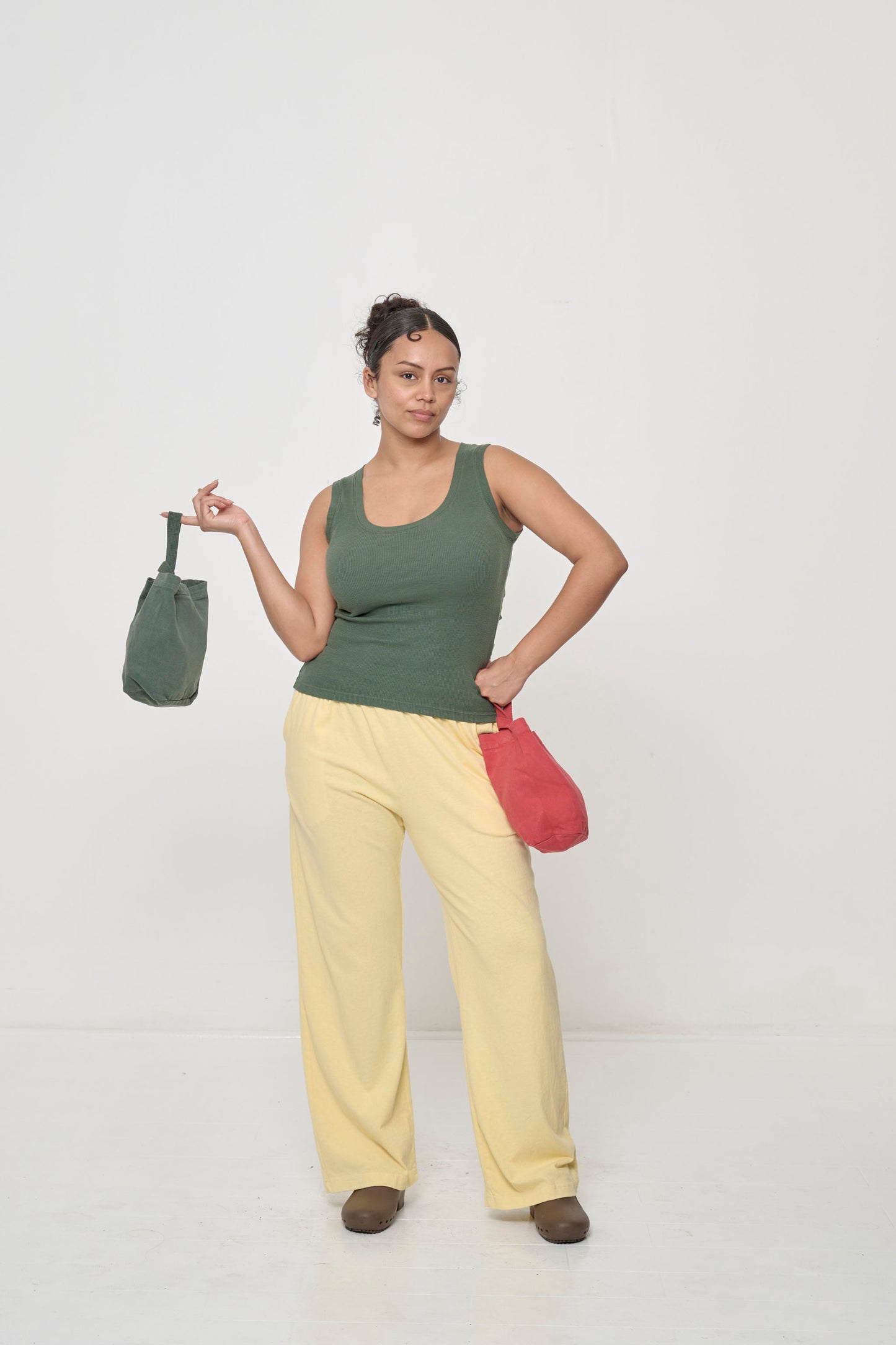 Woman in a Pine The Tank and French Butter Apartment Pants, holding a Pine and Cedar Loop Totes, one in each hand.