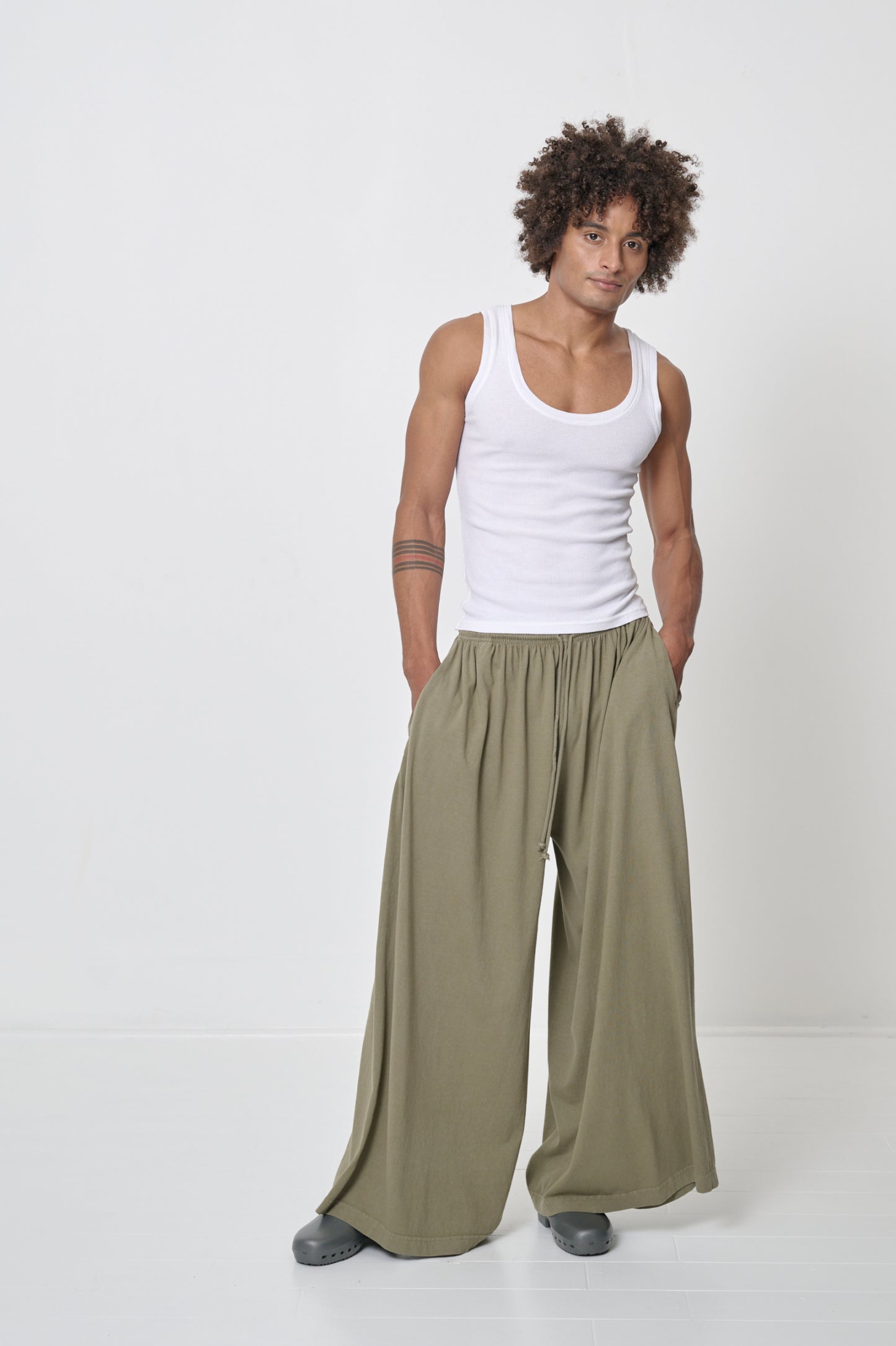 A person wearing a White The Tank with hands in the pockets of his khaki green Tubular Pants.