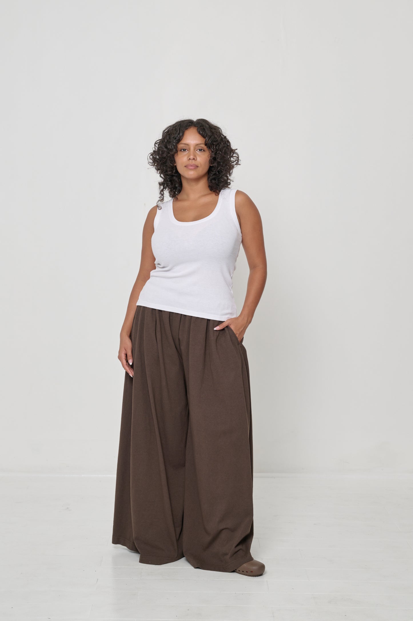 A woman wearing a White The Tank with one hand in the pocket of her brown Tubular Pants.
