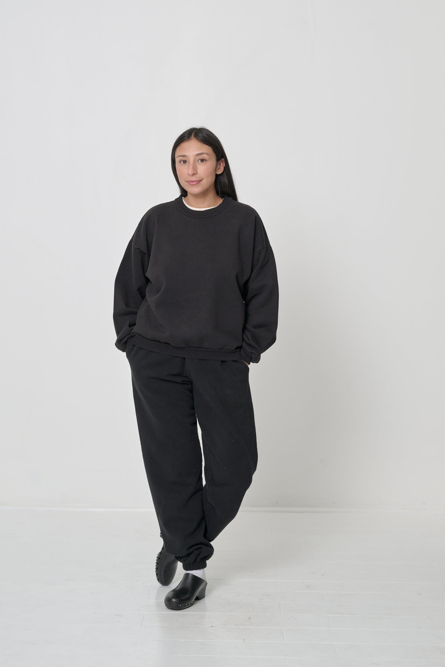 Front full length: woman in a Black Trash Crewneck, matching Everyday Shorts, White Squishy Socks and Black Calzuro Classic Clogs