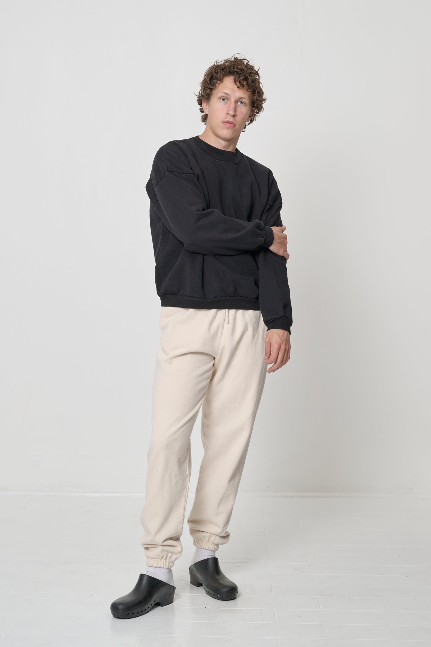 Front full length: man in a Black Trash Crewneck with one arm grabbing opposite elbow, showcasing sleeve's relaxed shape.