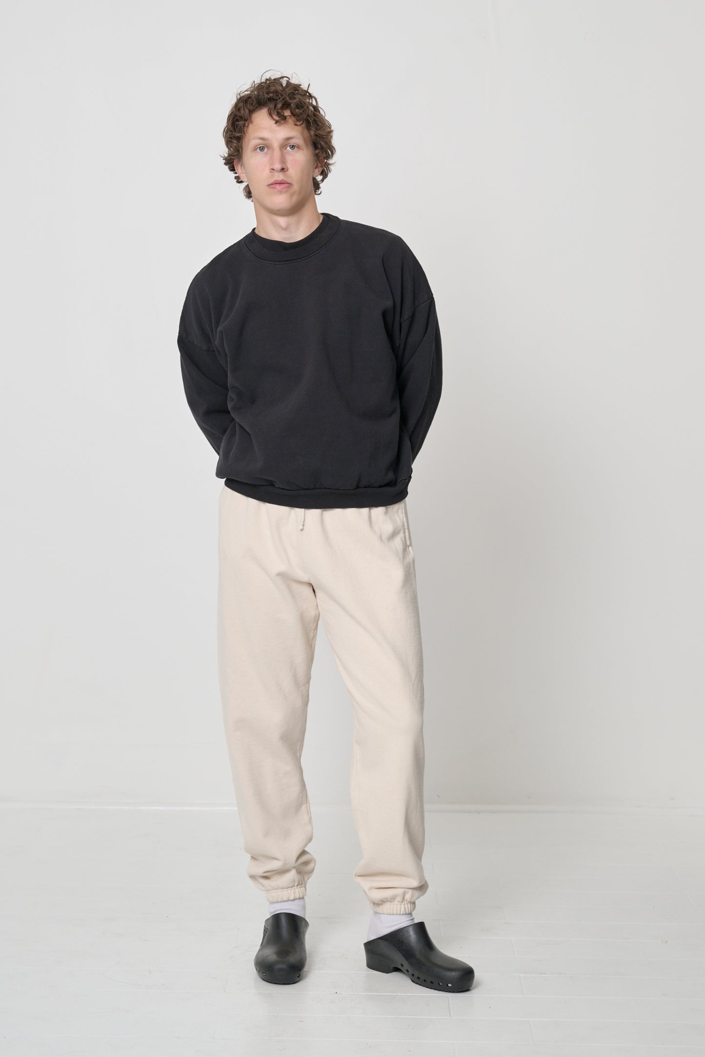 Front full length: man in a Black Trash Crewneck, Scour Trash Sweatpants and Black Calzuro Classic Clogs.