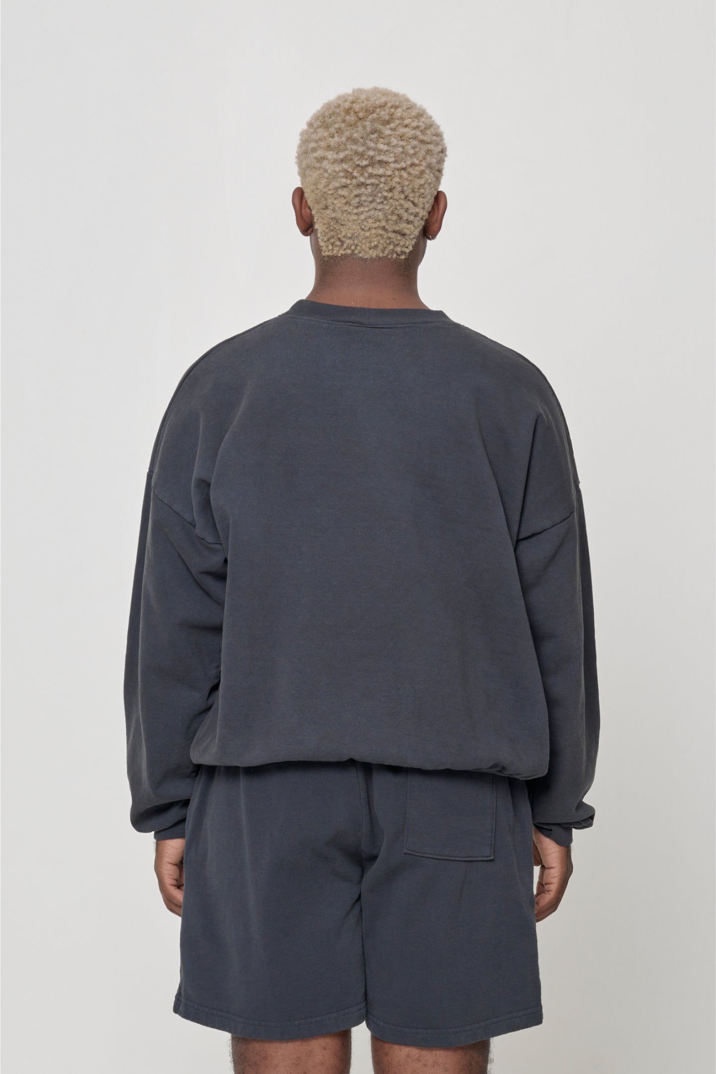 Slate Trash Crewneck, back view on a person. Relaxed throughout and rib hem is tucked under.