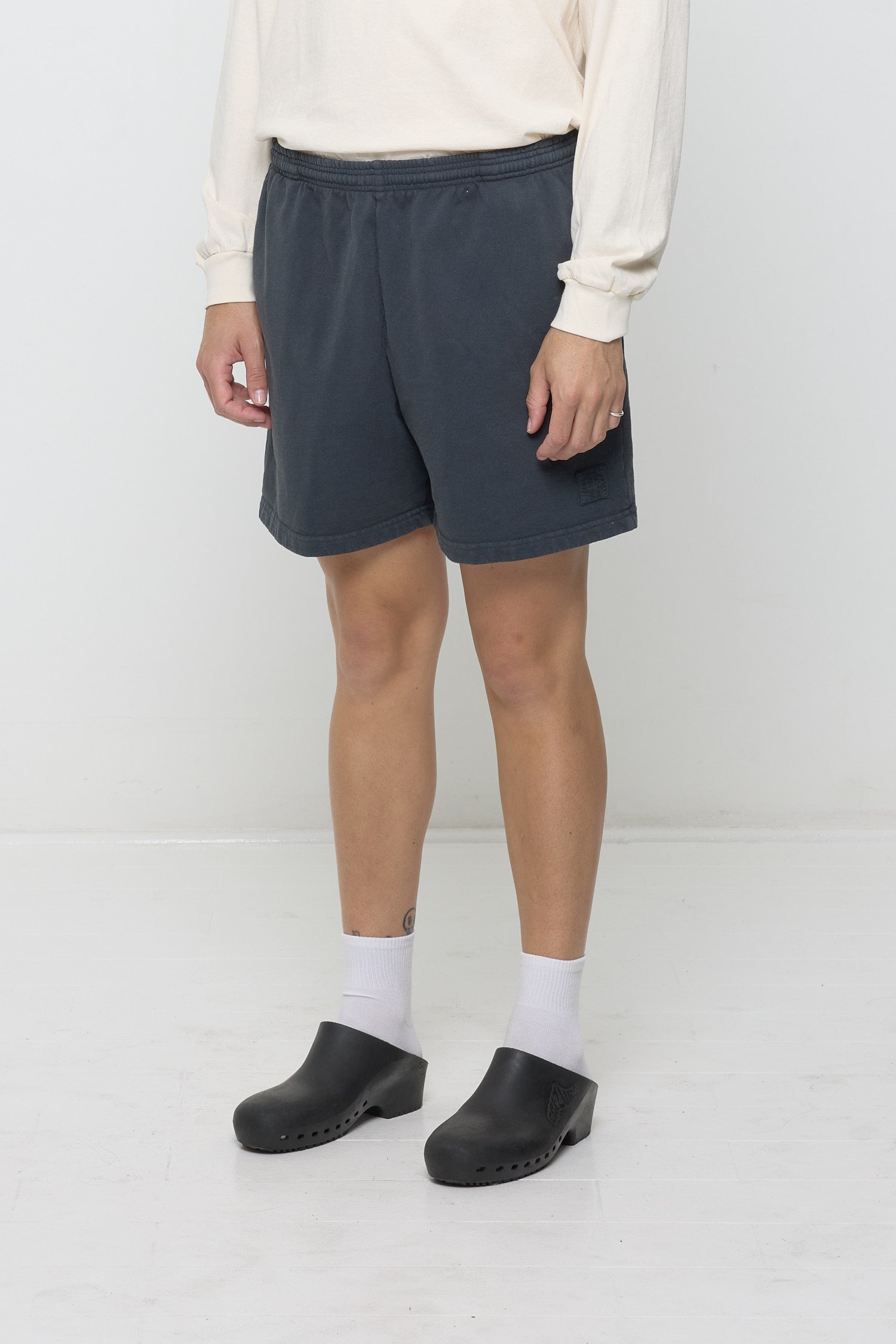 Slate Trash Fleece Everyday Shorts on a person, waist down, facing 45-degrees, with black E.W logo on bottom left leg.
