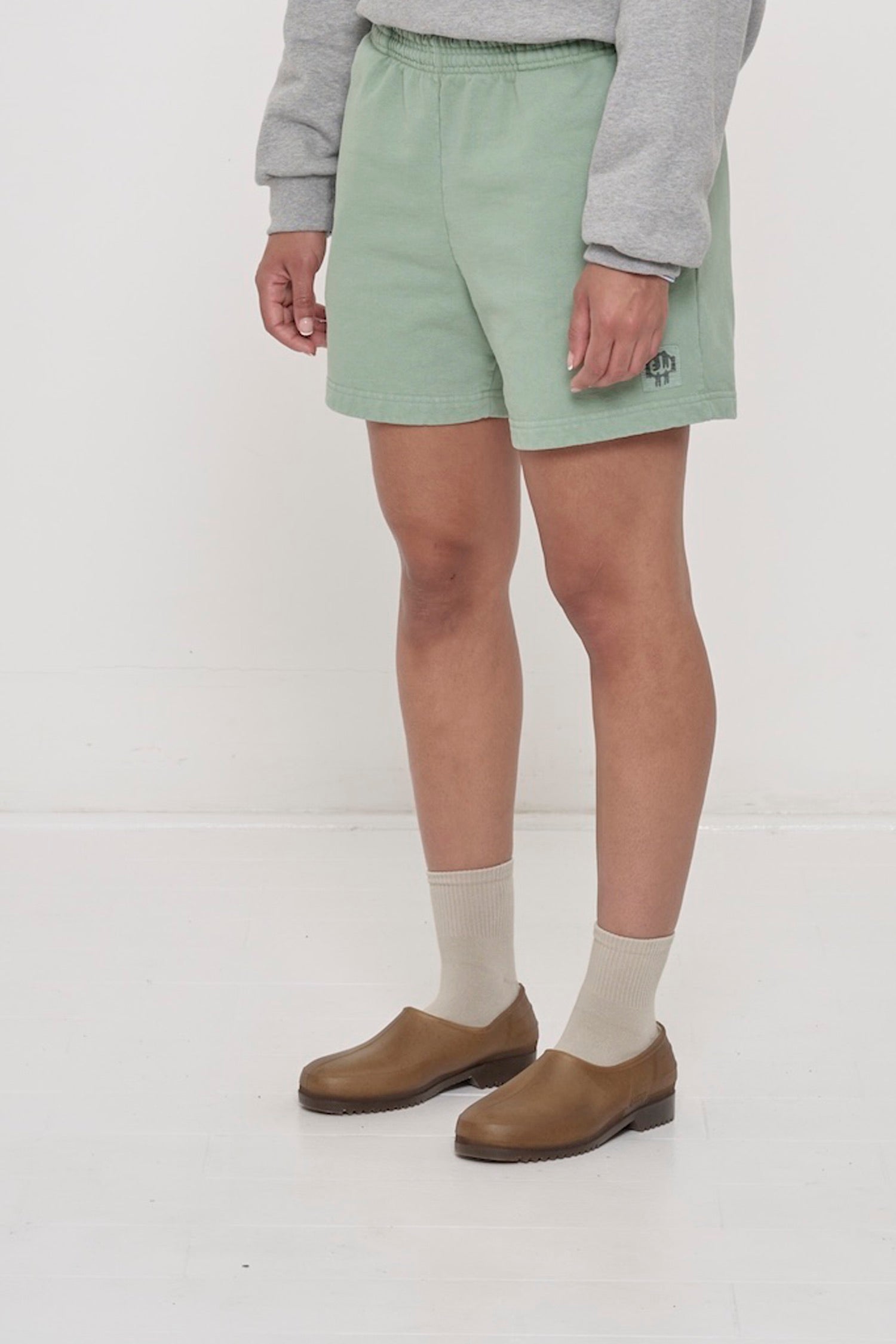 Wasabi Trash Fleece Everyday Shorts on a person, waist down, facing 45-degrees, with grey E.W logo on bottom left leg.