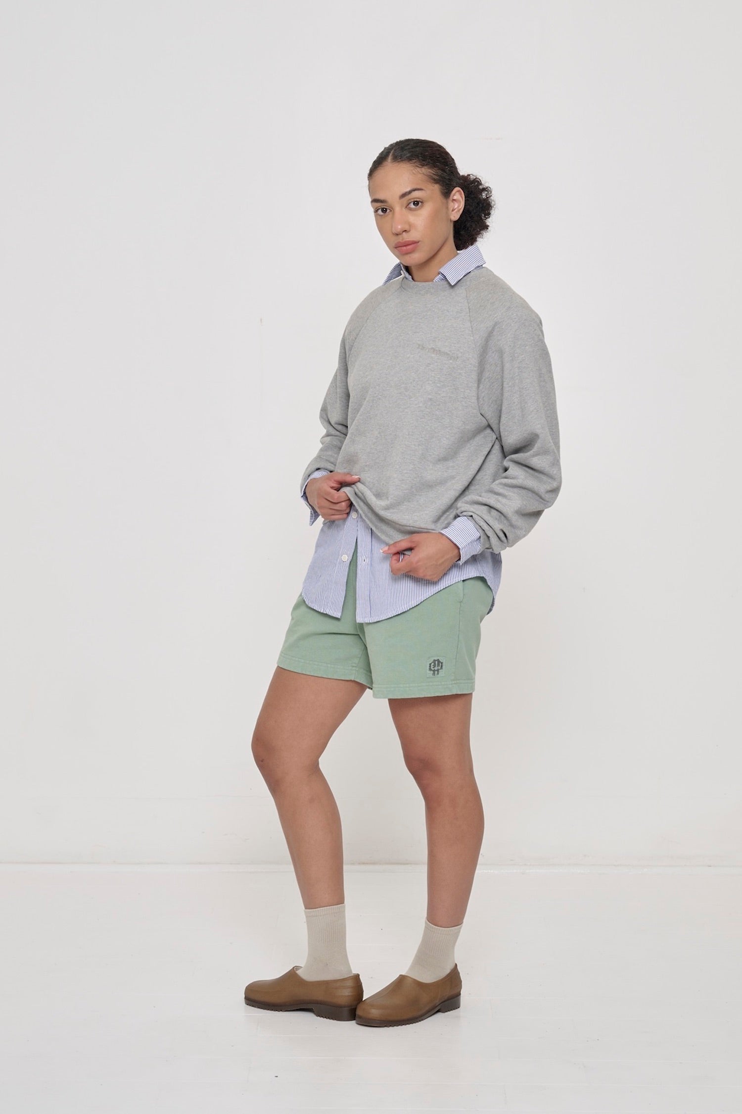 Woman in Wasabi Trash Fleece Everyday Shorts and Heather Trash Raglan, pulling hem of the sweatshirt.