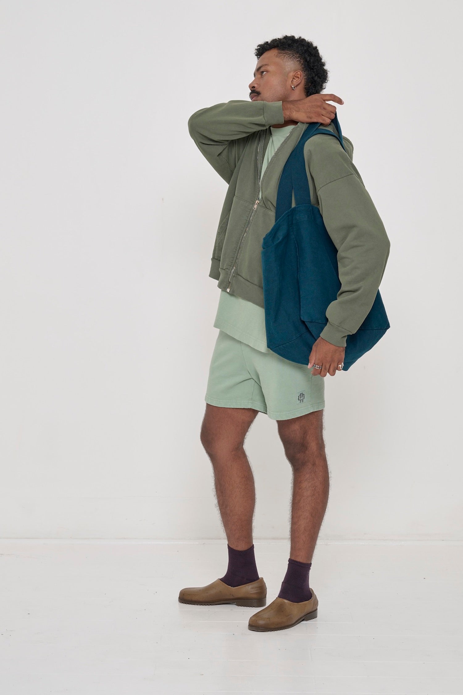 Profile: a man in Wasabi Trash Fleece Everyday Shorts pulling a Juniper Big Tote onto his shoulder.