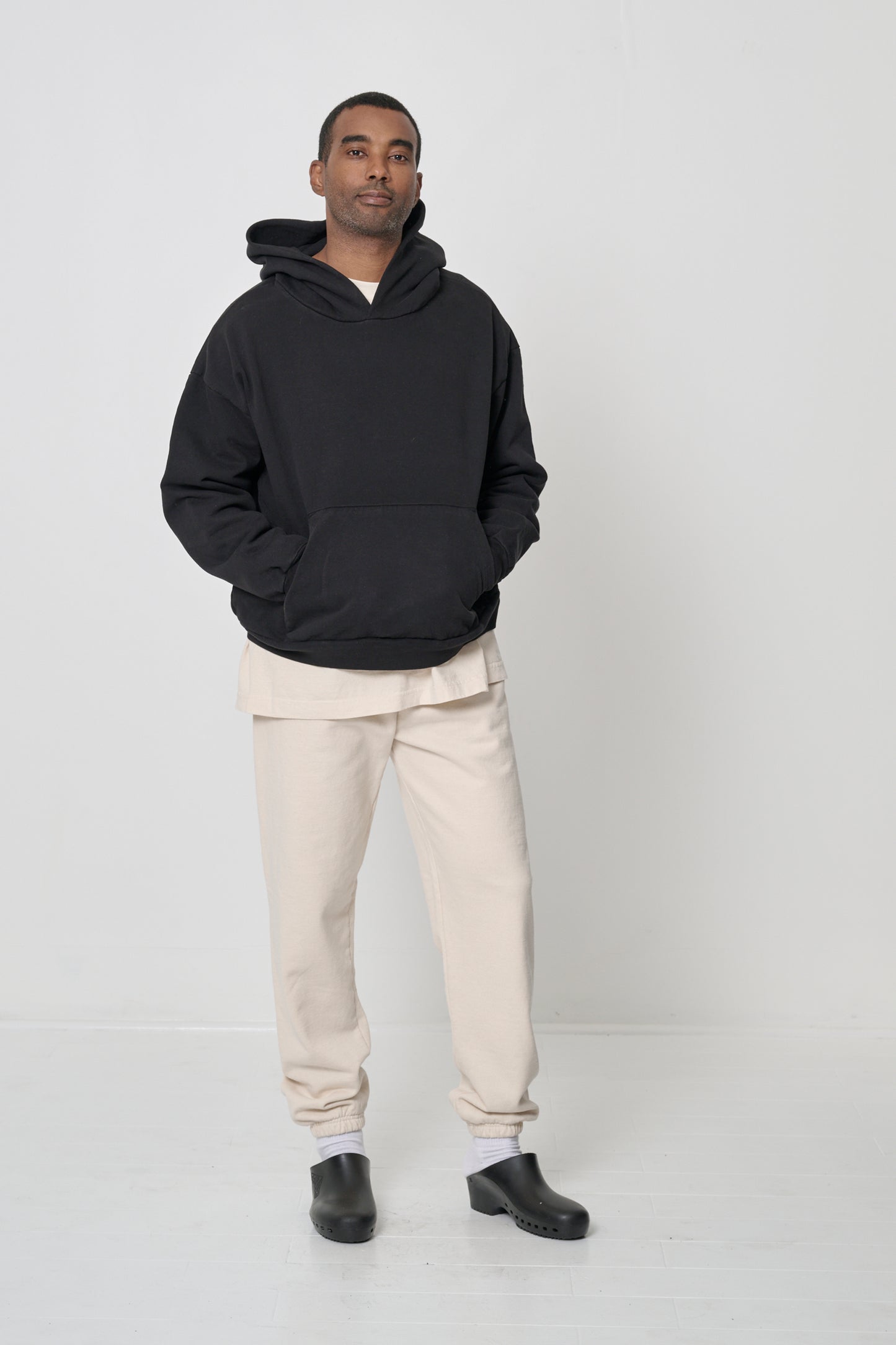 Front full length view: man wearing a Black Trash Hoodie with hands in the kangaroo pocket.