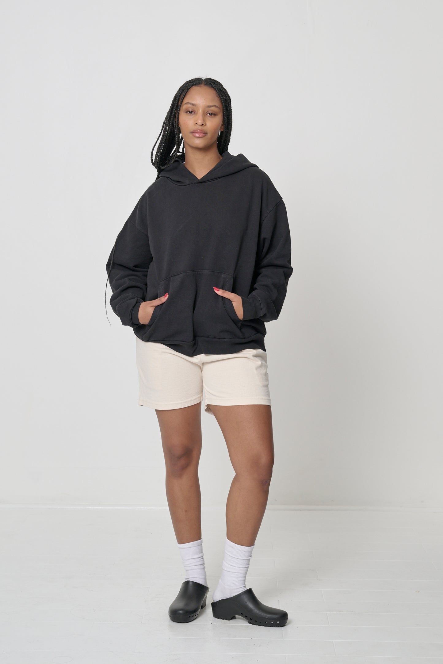 Front full length: woman wearing a Black Trash Hoodie with hands in the kangaroo pocket